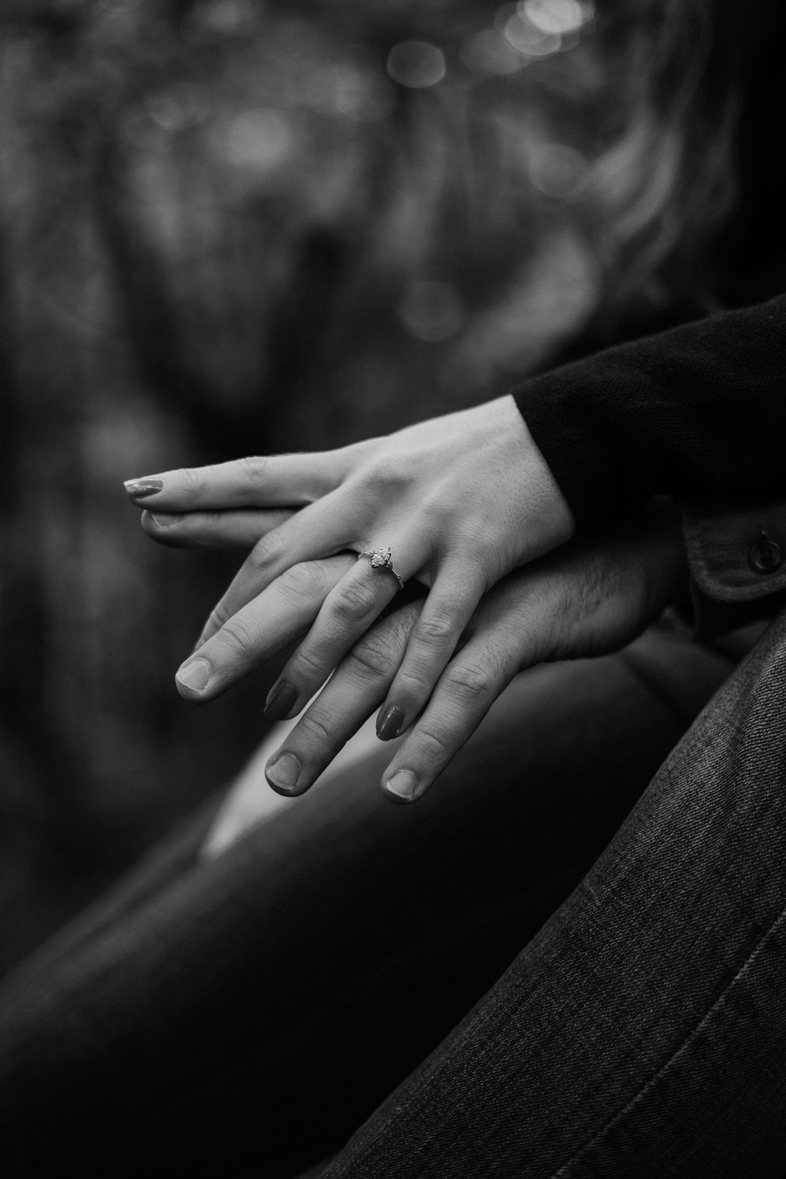 Close-up black and white photo of hands with an engagement ring against a blurred background.