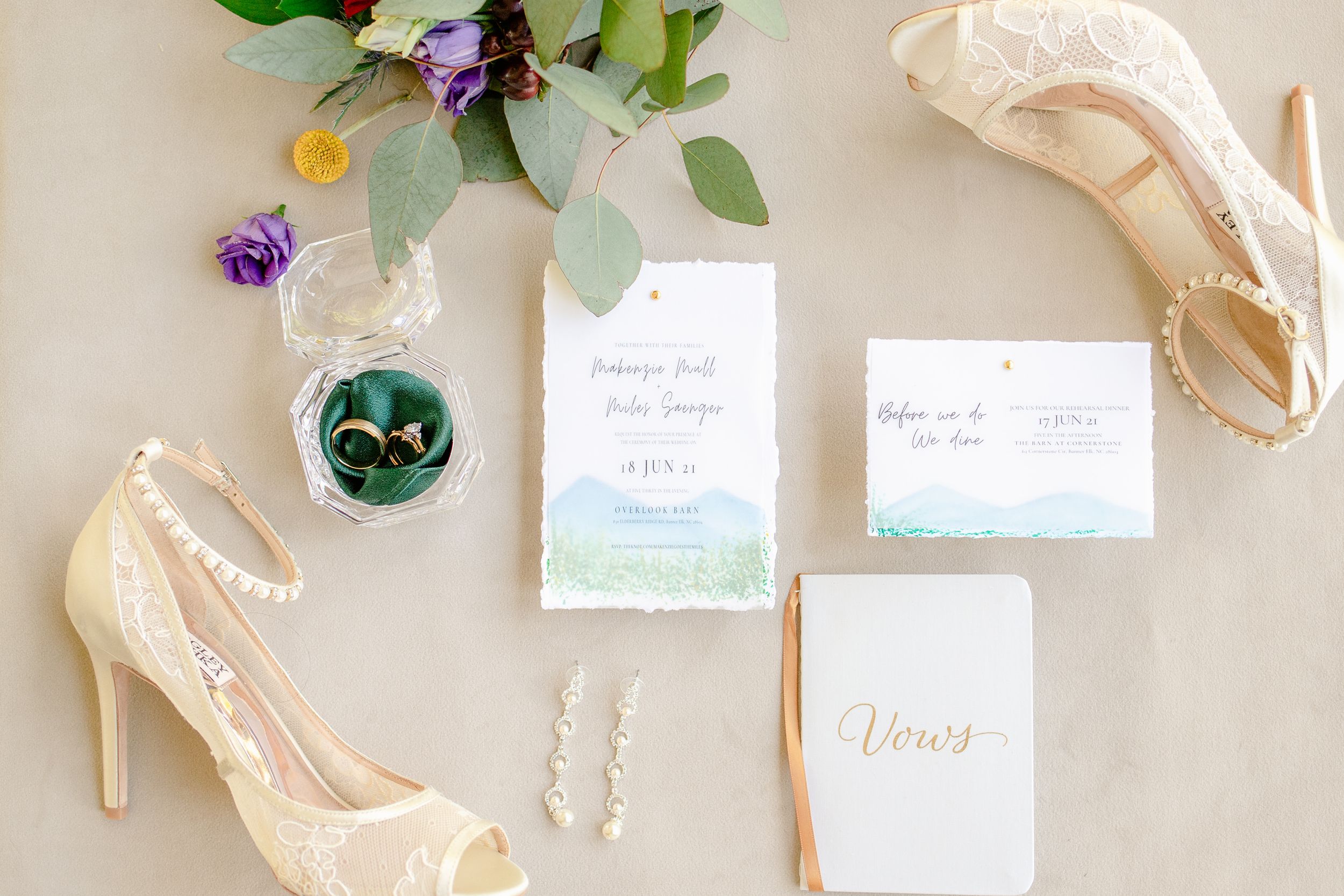 Wedding detail shot with cream heels, floral invitations and crystal ring box on light background.