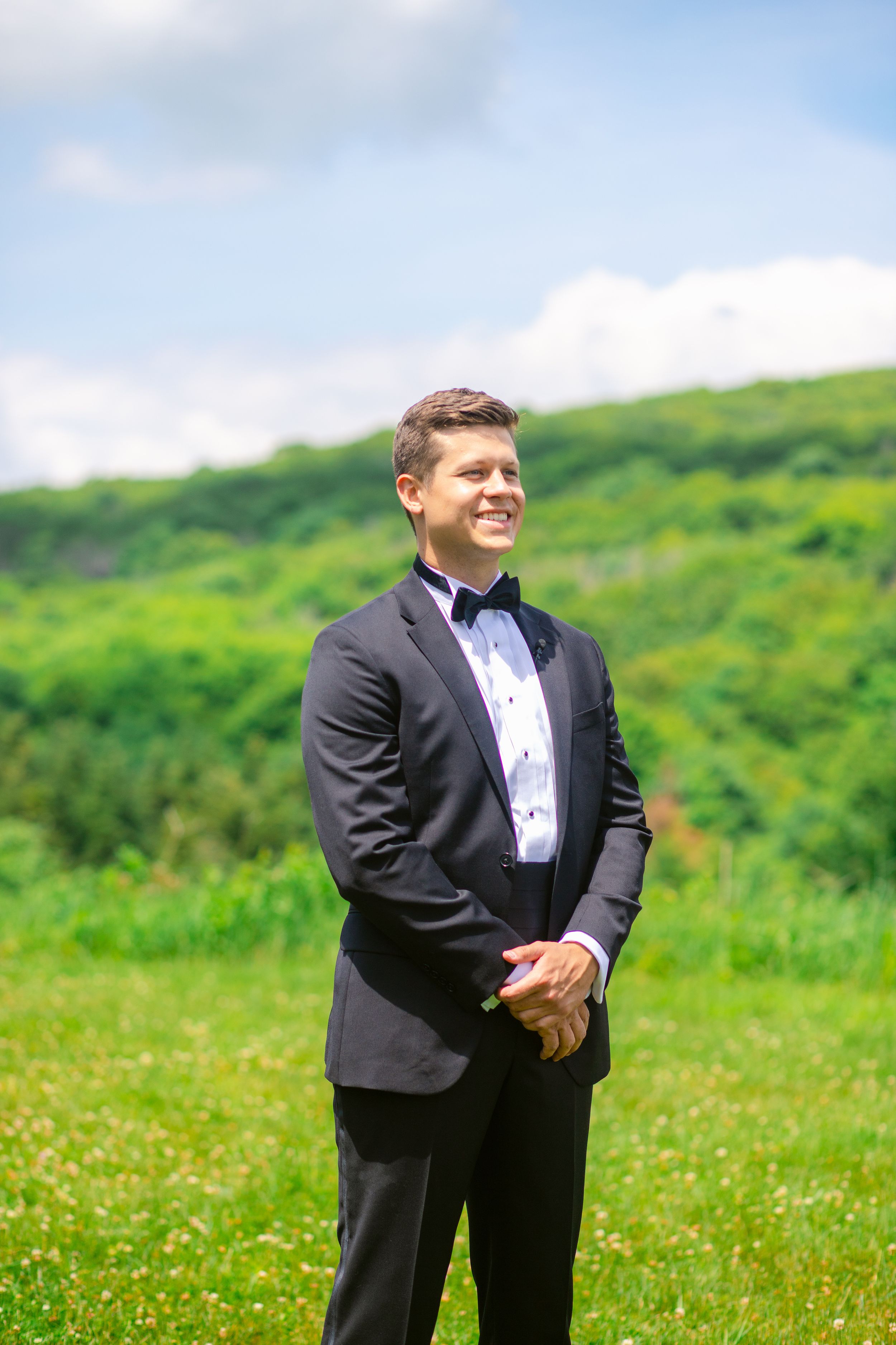 Outdoor portrait in formal attire against a lush green mountain backdrop.