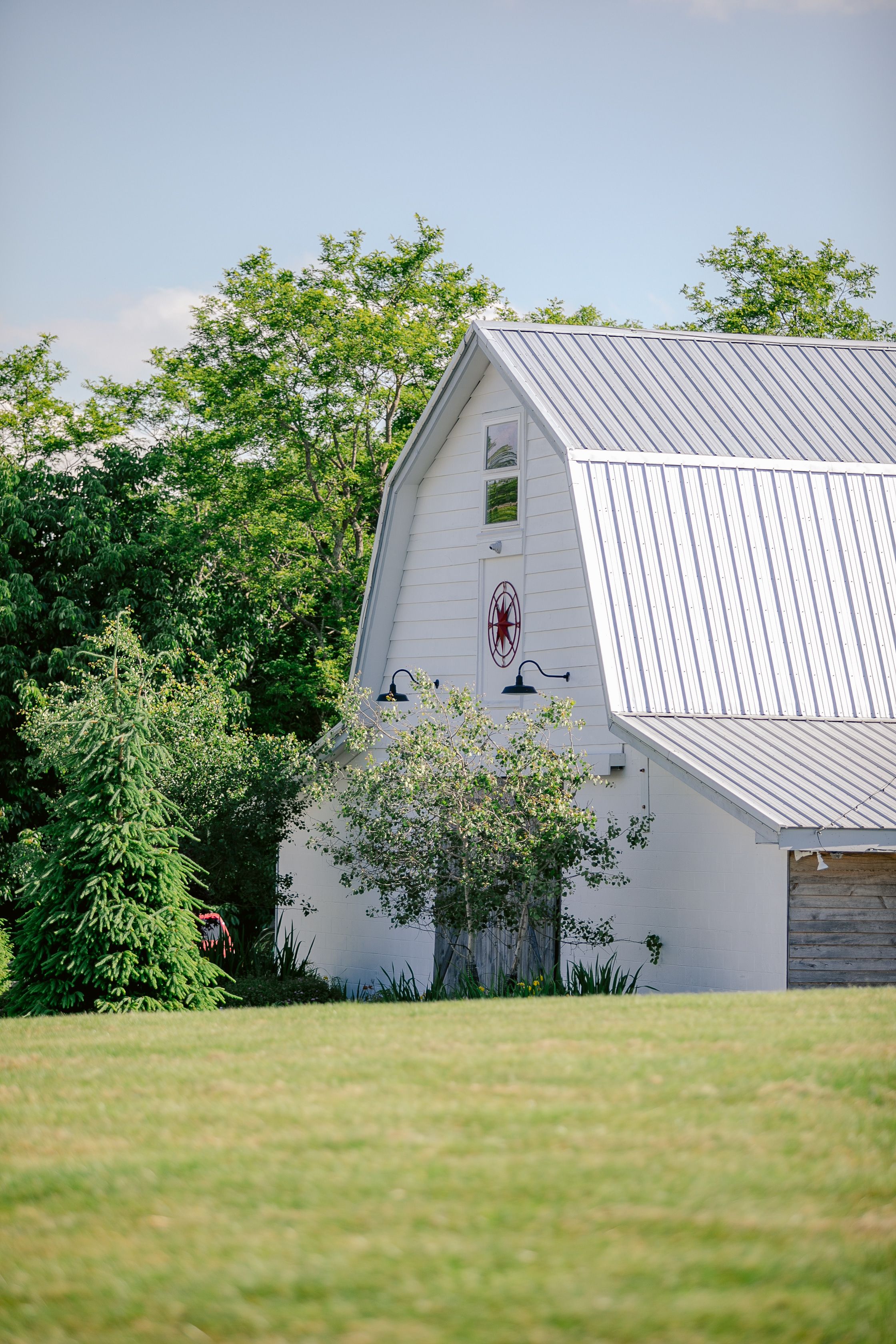 White barn-style building with metal roof and decorative elements on a green lawn.