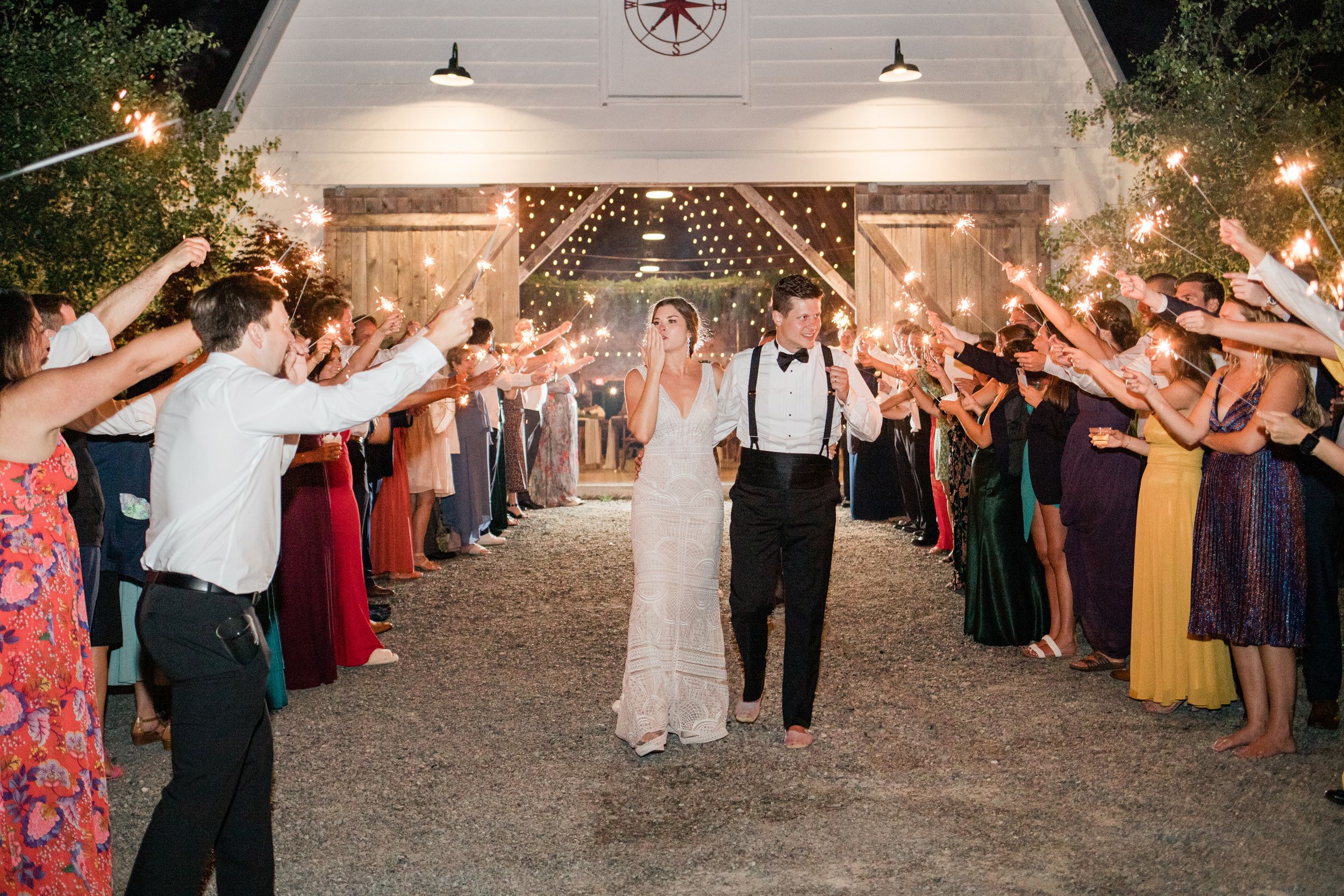 Couple exits wedding venue through sparkler tunnel lined with guests in colorful attire.