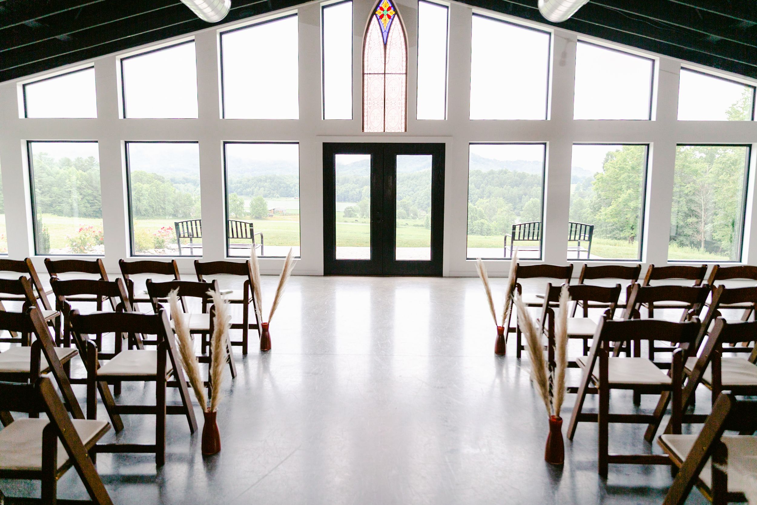 Large bright event venue with wooden floors and floor-to-ceiling windows overlooking scenic landscape.