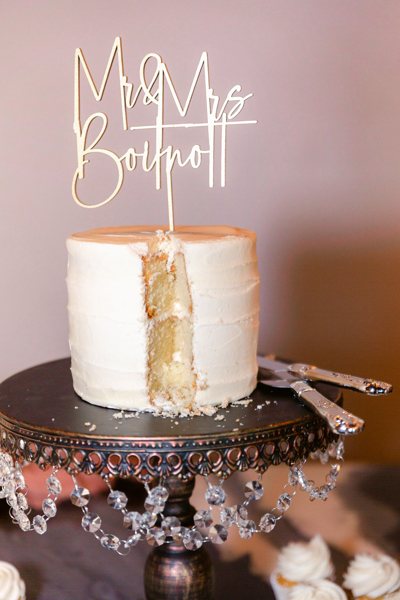 White wedding cake displayed on an ornate crystal-trimmed black cake stand.