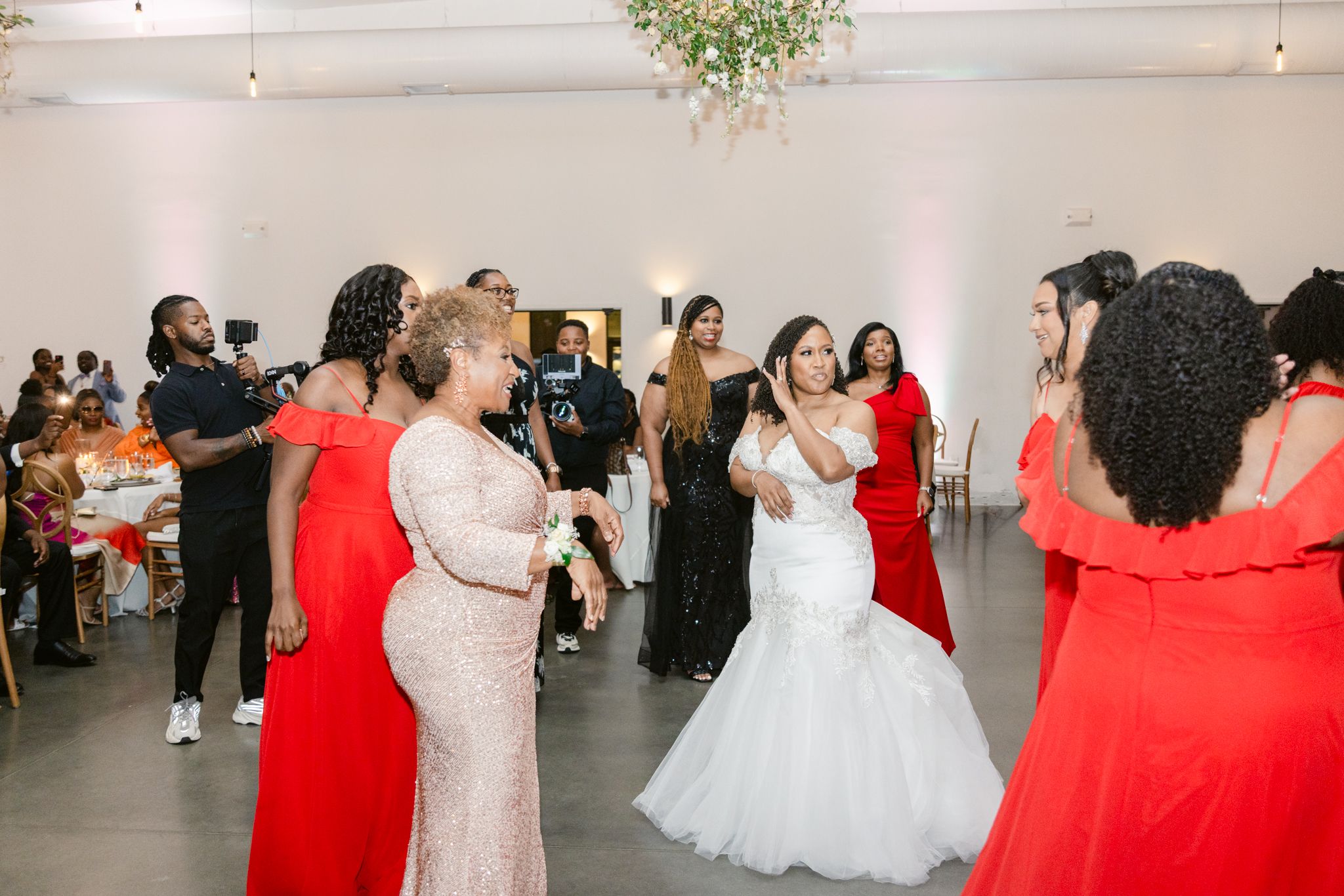 Wedding party members in red and white dresses dancing together at a modern reception venue.