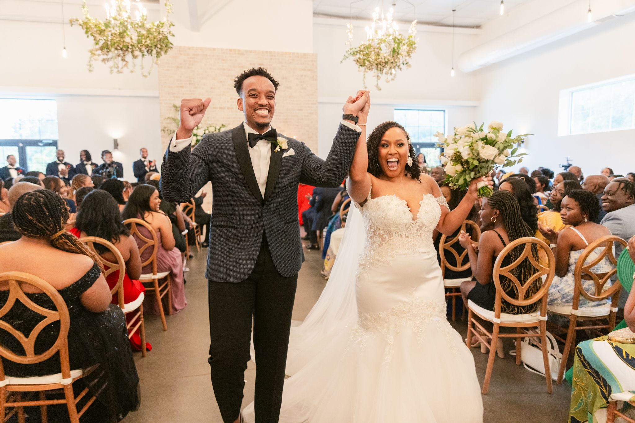 Joyful newlyweds make their grand exit through the aisle with guests cheering in a modern venue.