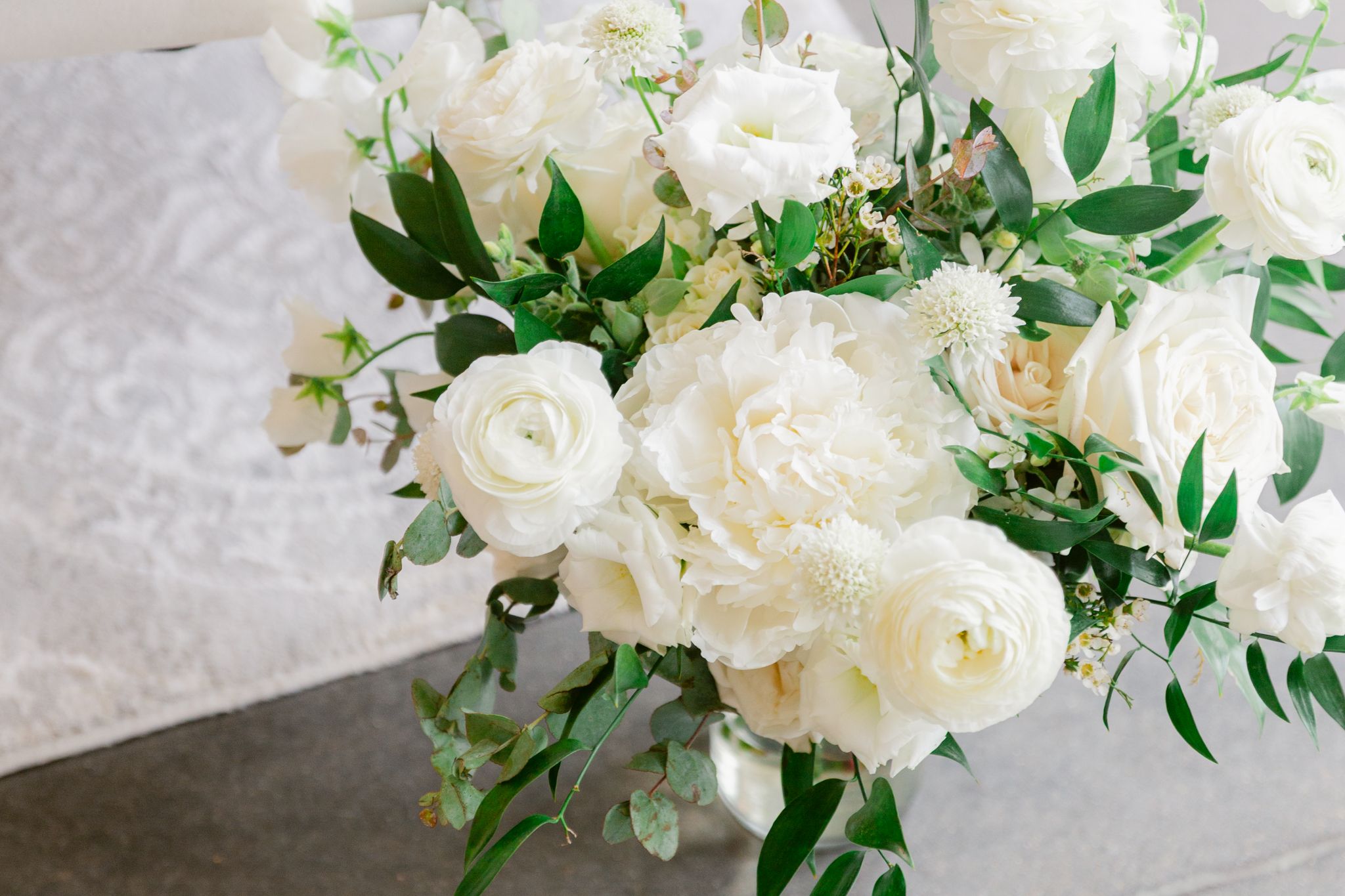 Elegant white roses and delicate greenery arranged in a romantic floral wedding centerpiece on a light background.