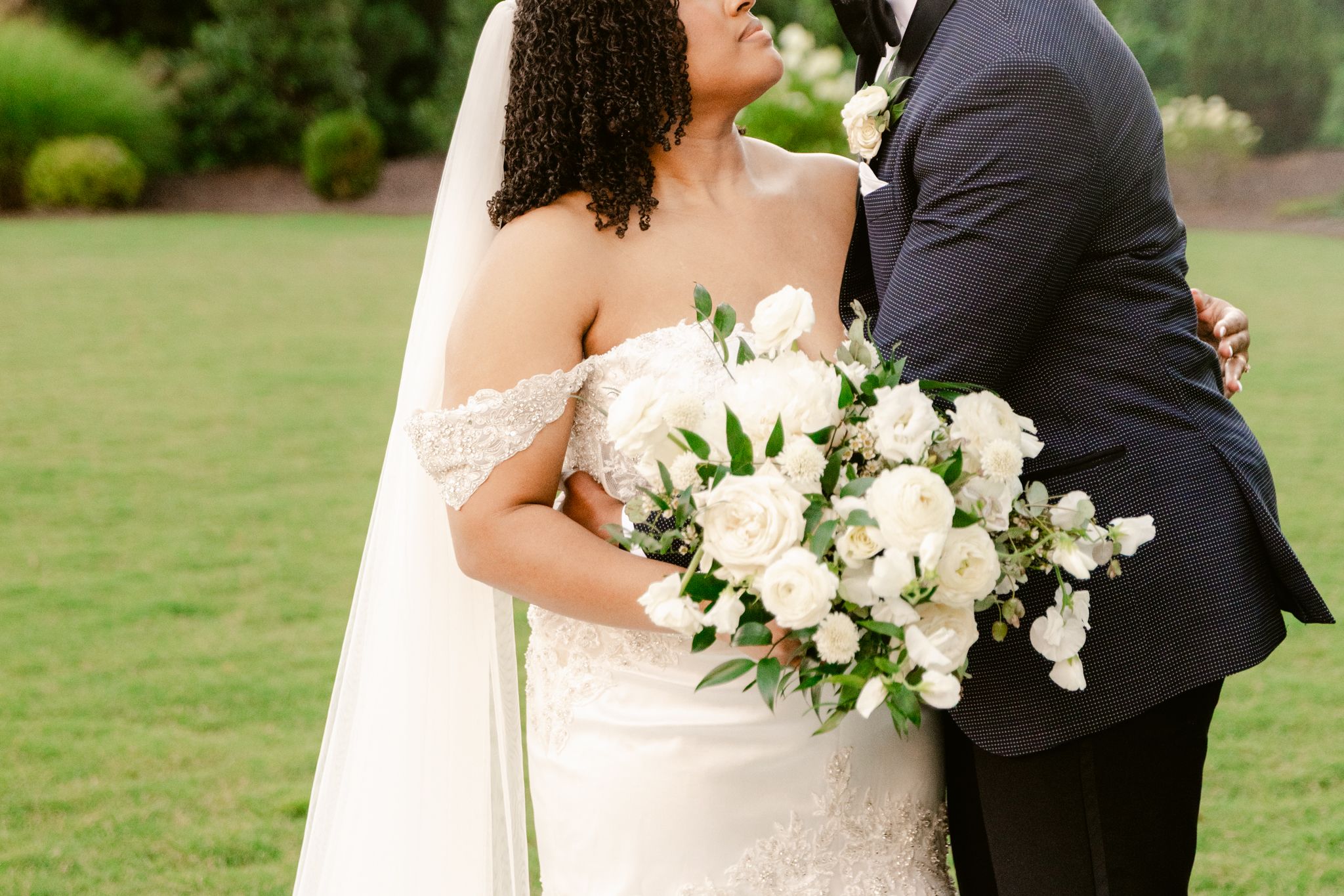 A couple shares an intimate moment on their wedding day in a lush garden setting with white floral bouquet.