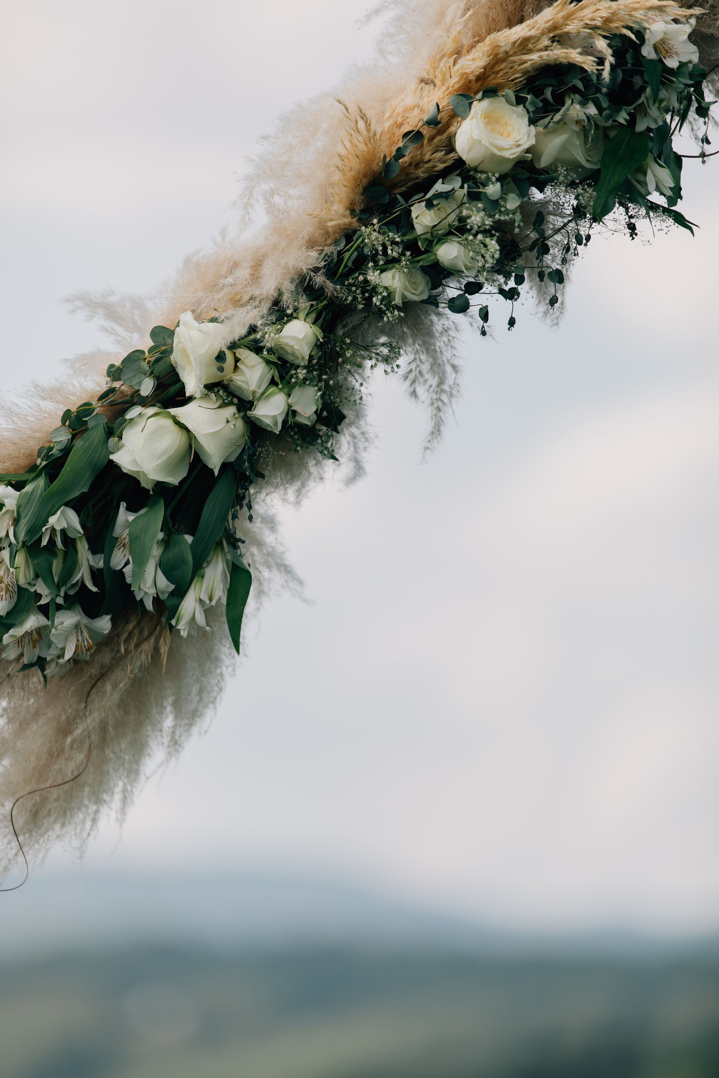 Floral wedding arch decoration with white roses and pampas grass against a mountain backdrop.