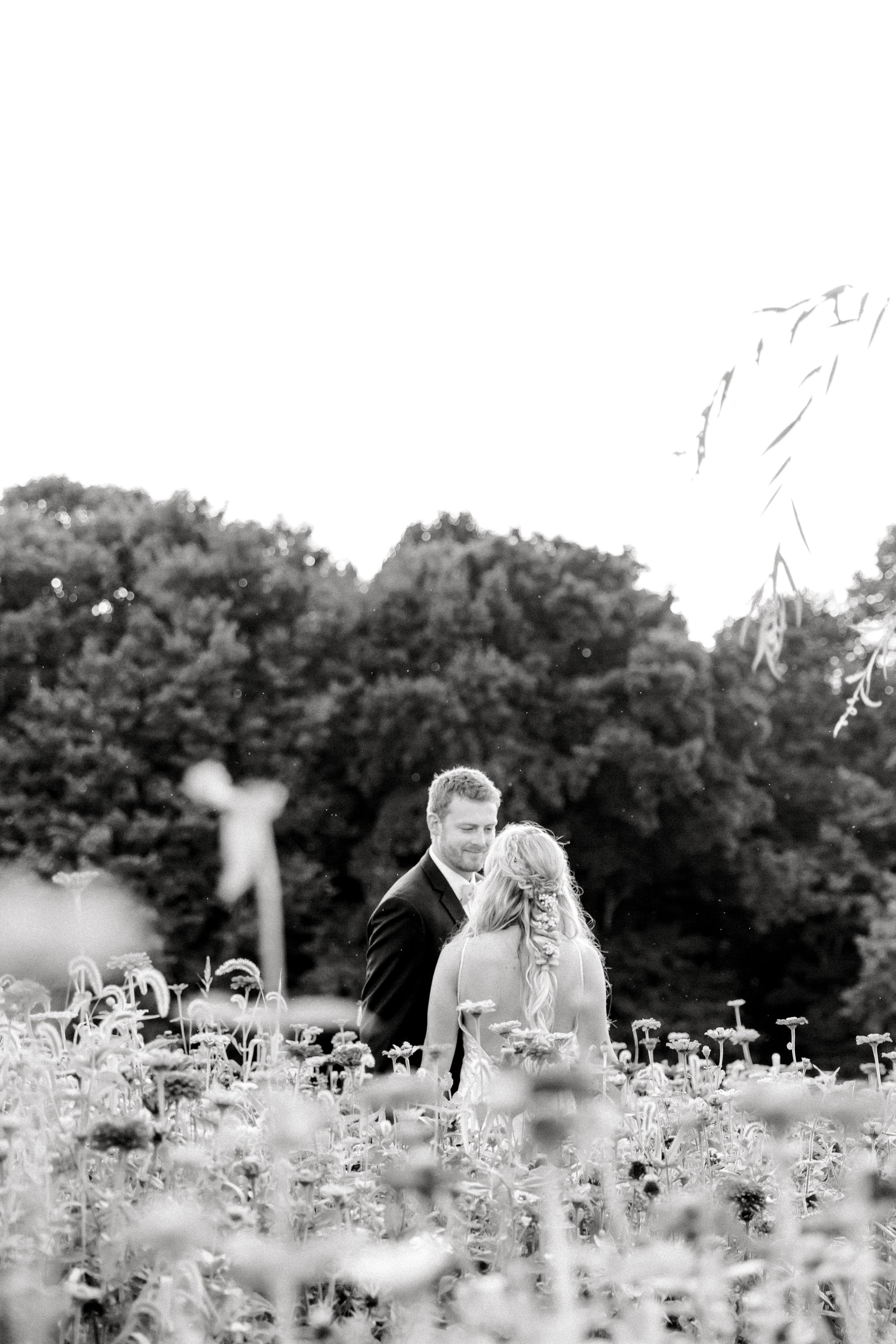 Black and white portrait of newlyweds among wildflowers in a meadow.