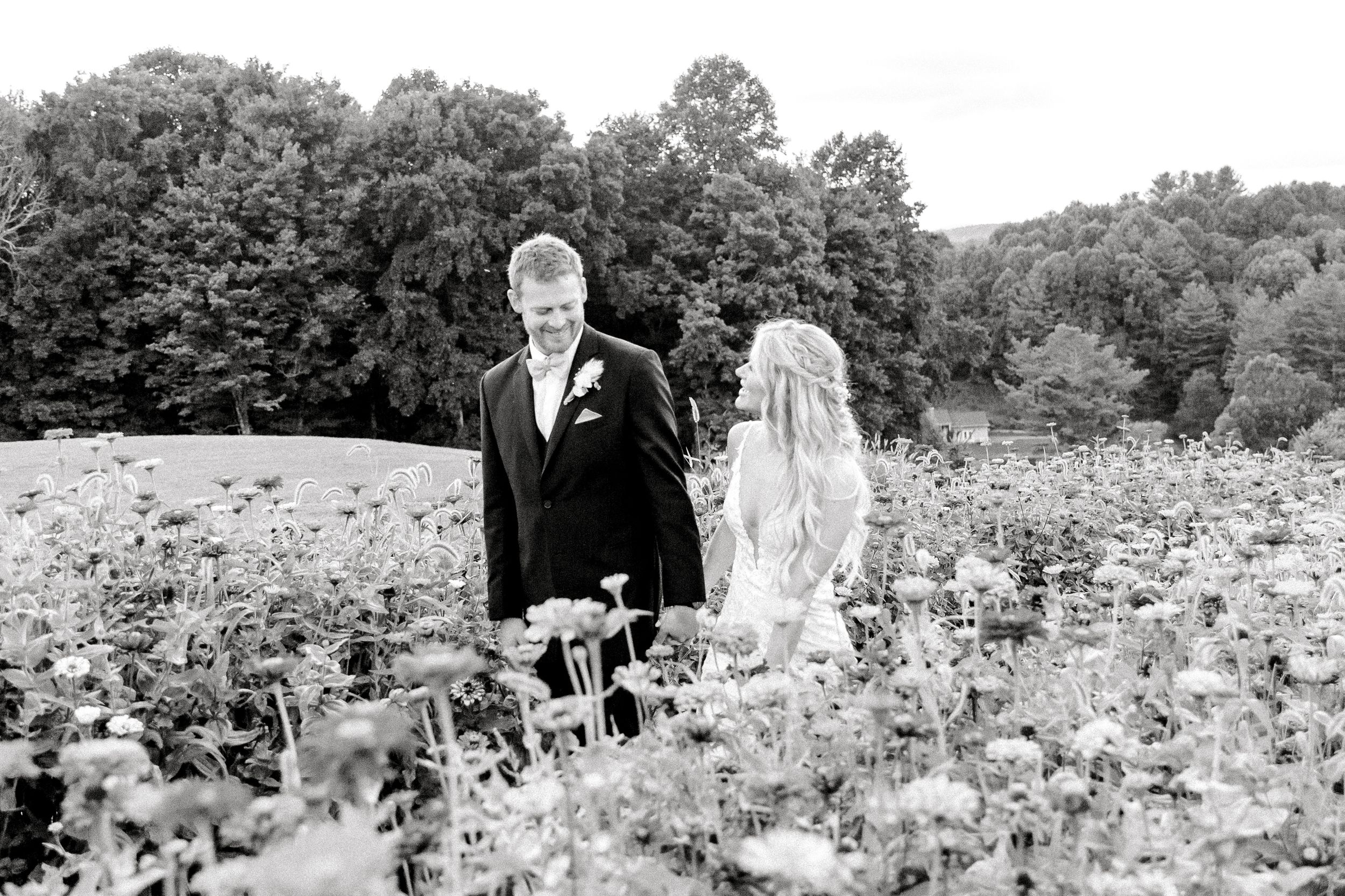 Black and white wedding photo of couple standing in wildflower meadow.