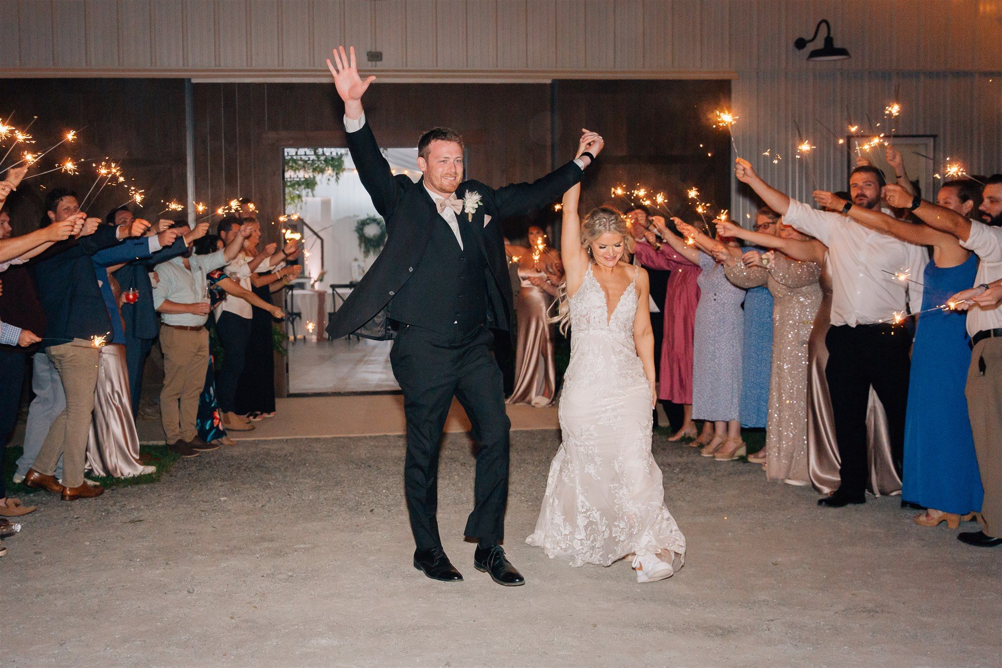 Celebrating newlyweds raise their arms in triumph as guests form a sparkler-lit pathway.