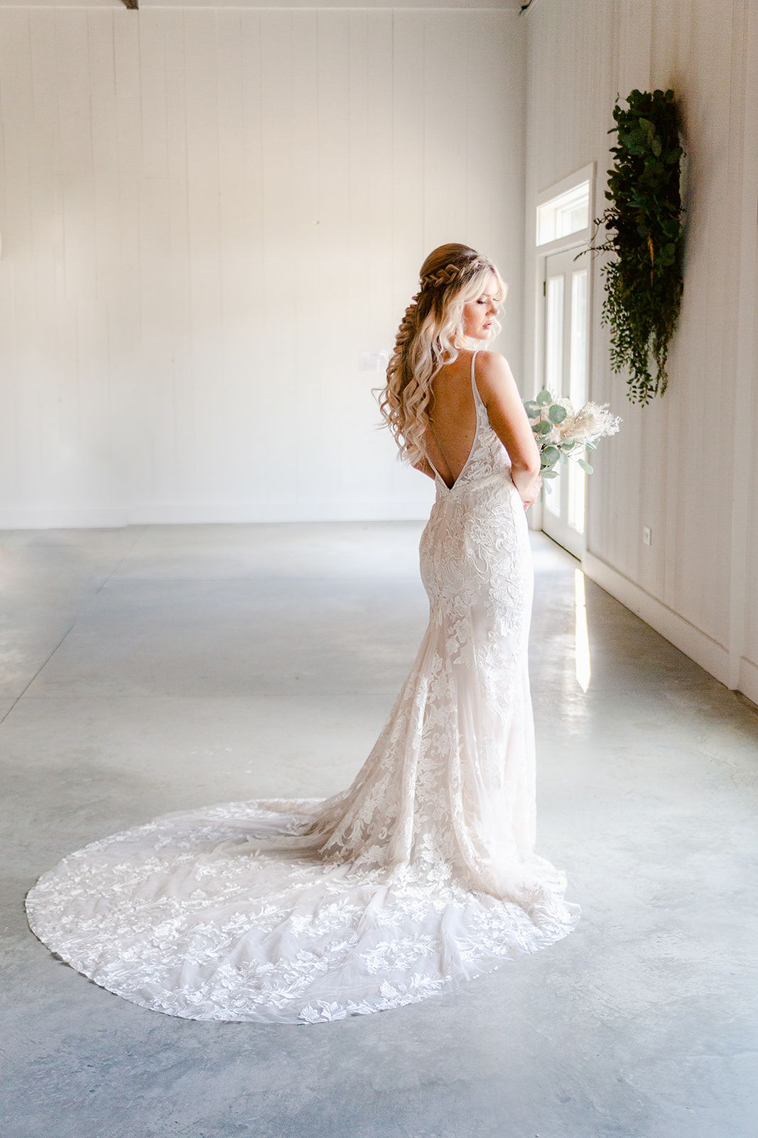 Lace wedding gown with long train displayed in minimalist white room.