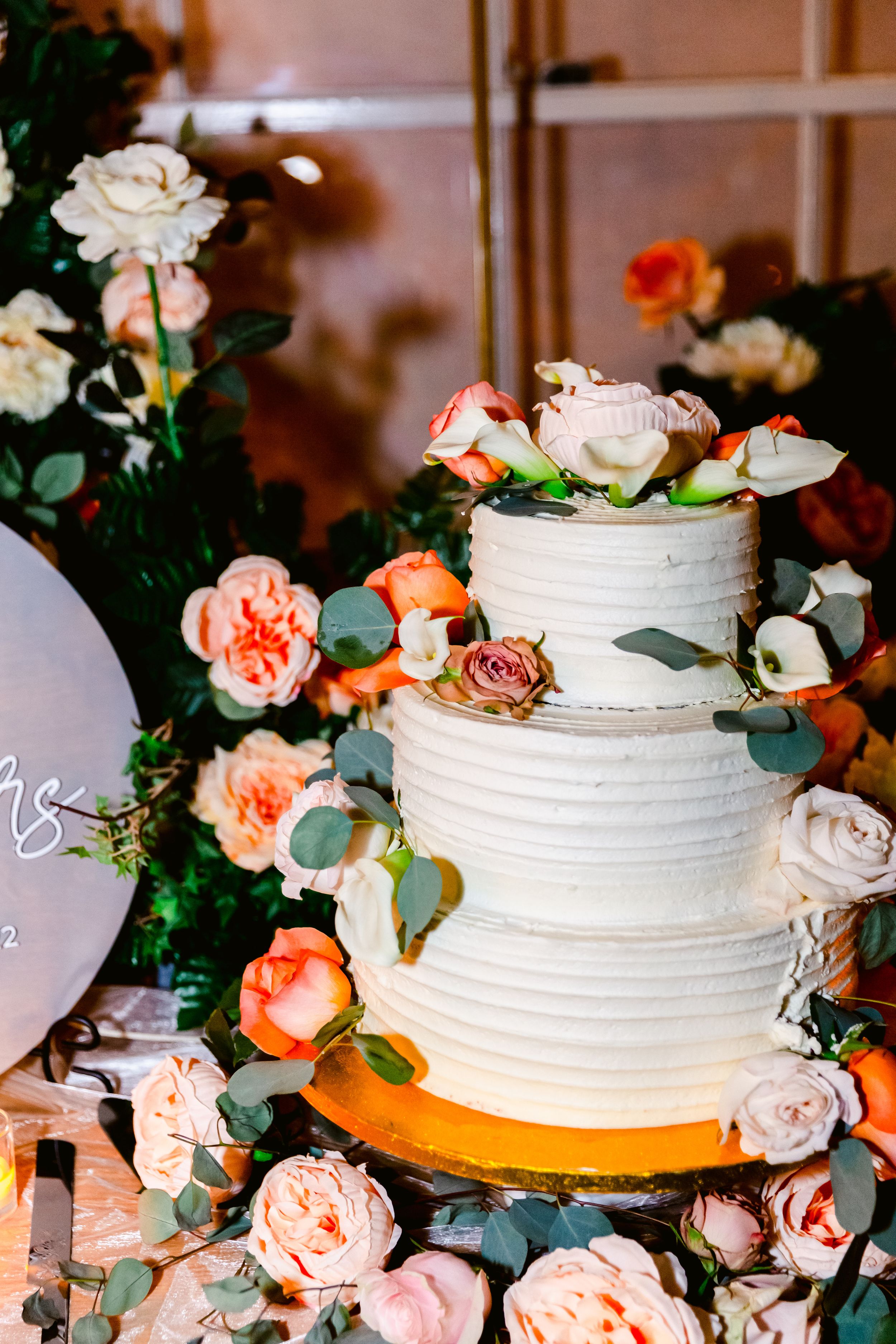 Three-tiered white wedding cake decorated with peach roses and eucalyptus leaves on a wooden table.