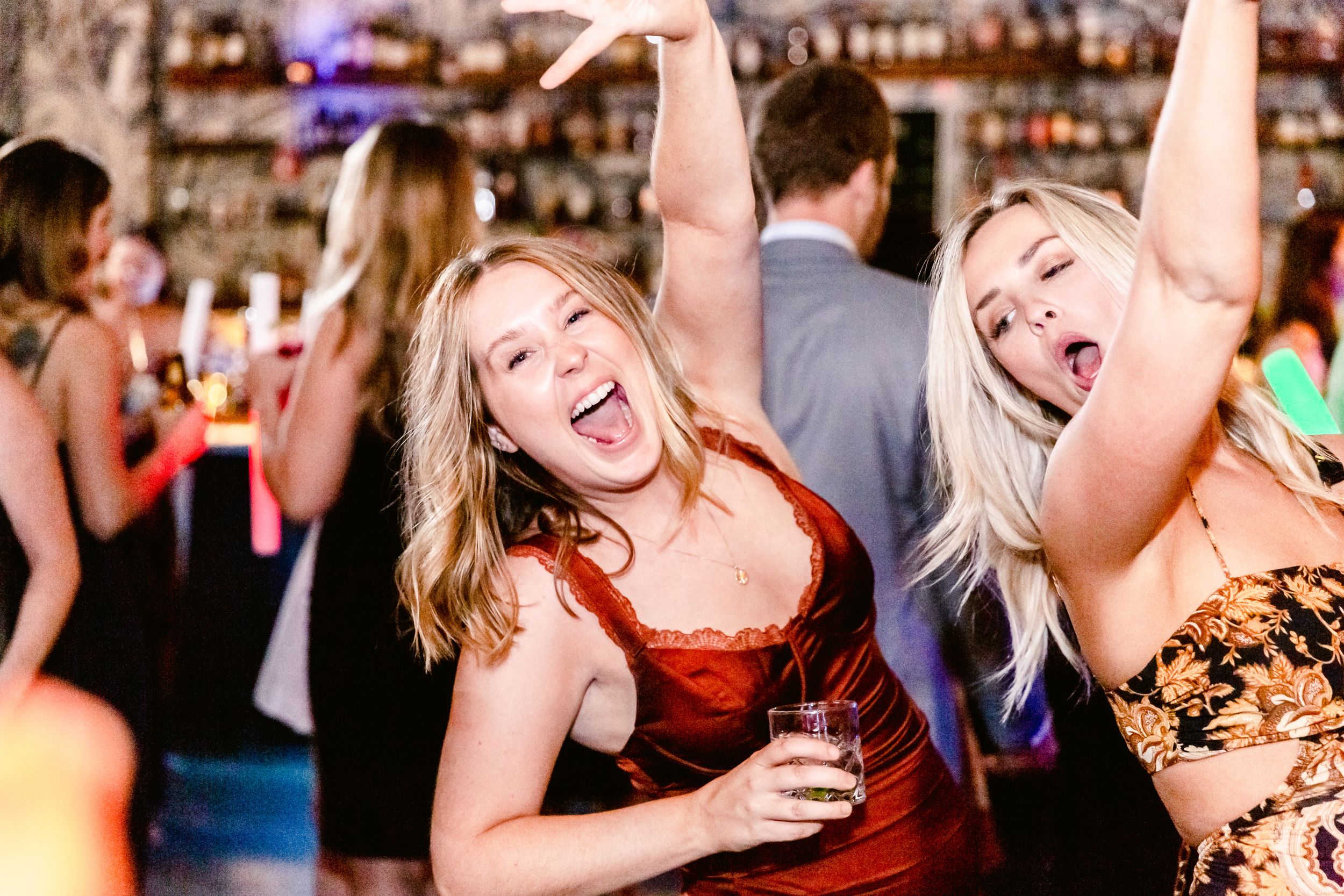 People dancing and celebrating together at a lively bar or party venue with colorful lighting in the background.