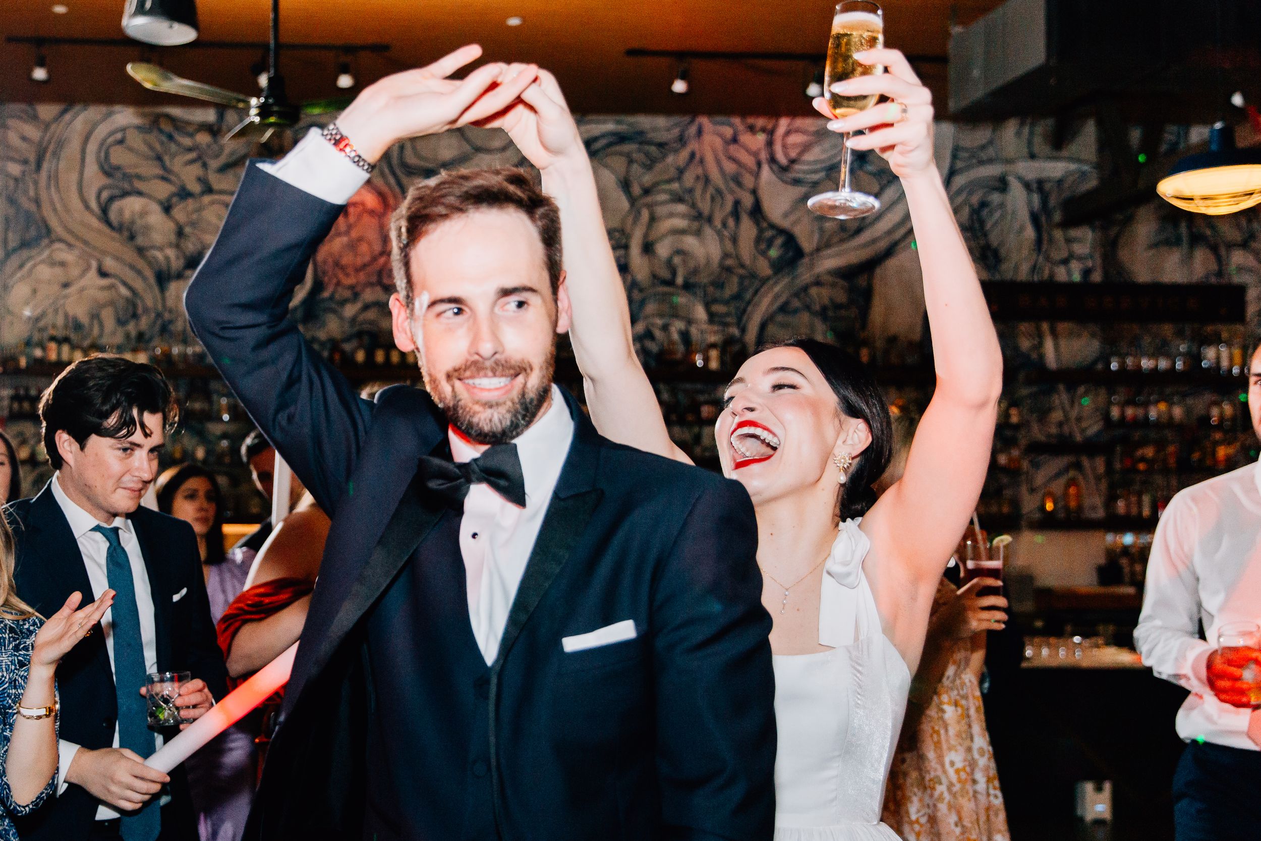 People dancing and celebrating at a lively wedding reception in a dimly lit venue with rustic decor.