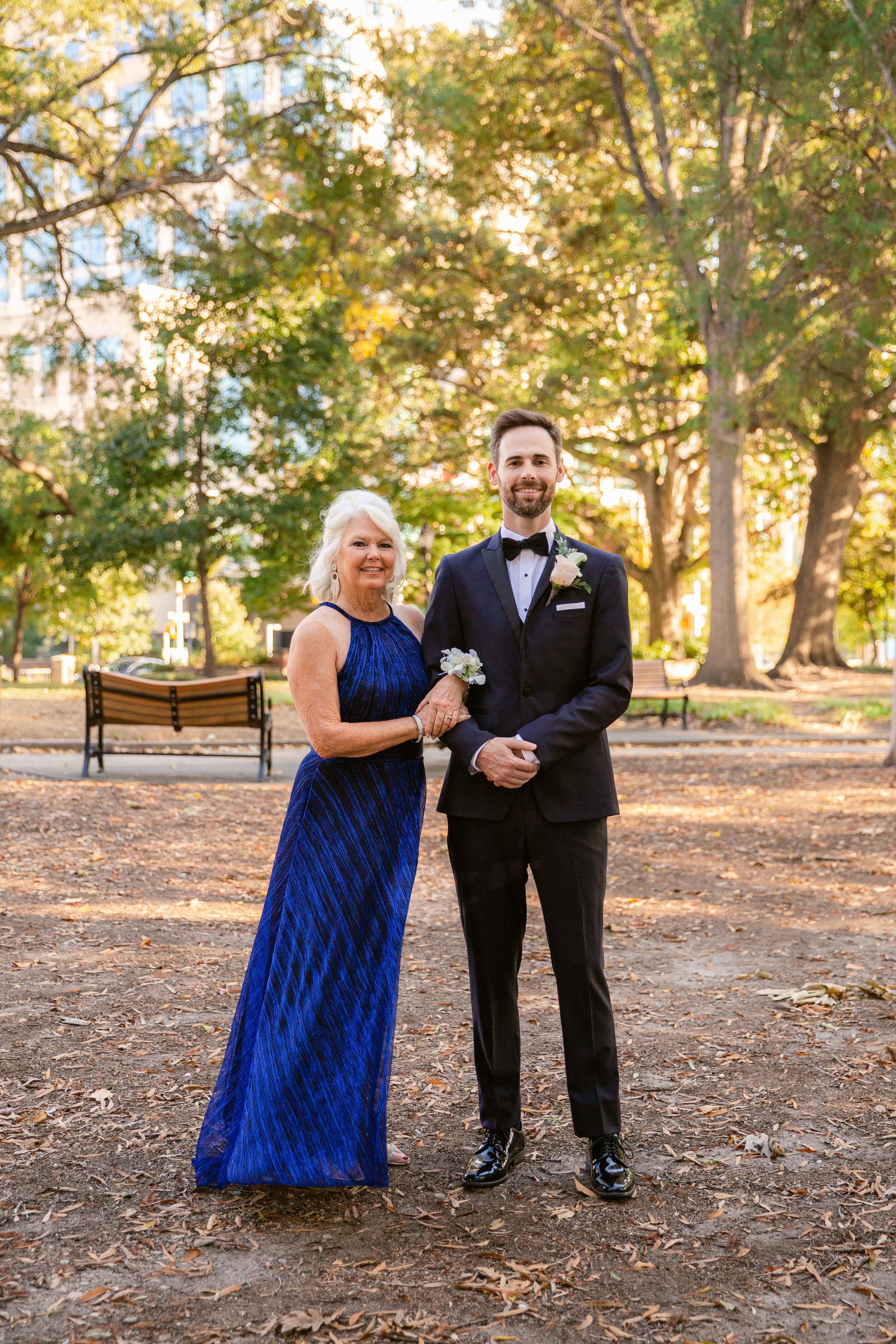 Formal couple poses outdoors in autumn park setting with blue gown and black tuxedo.