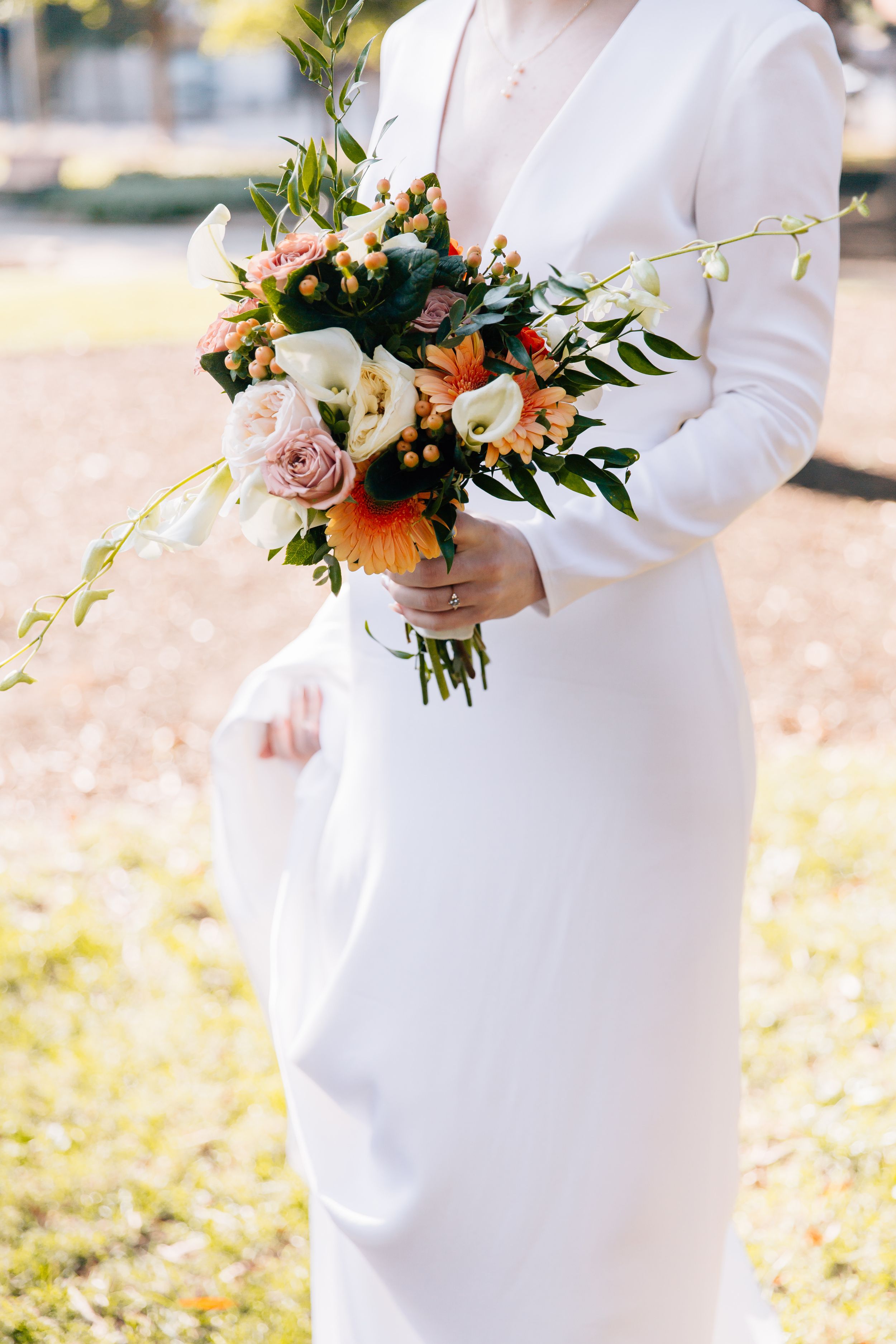 A close-up of a bridal bouquet featuring peach and blush flowers with greenery against a white dress.