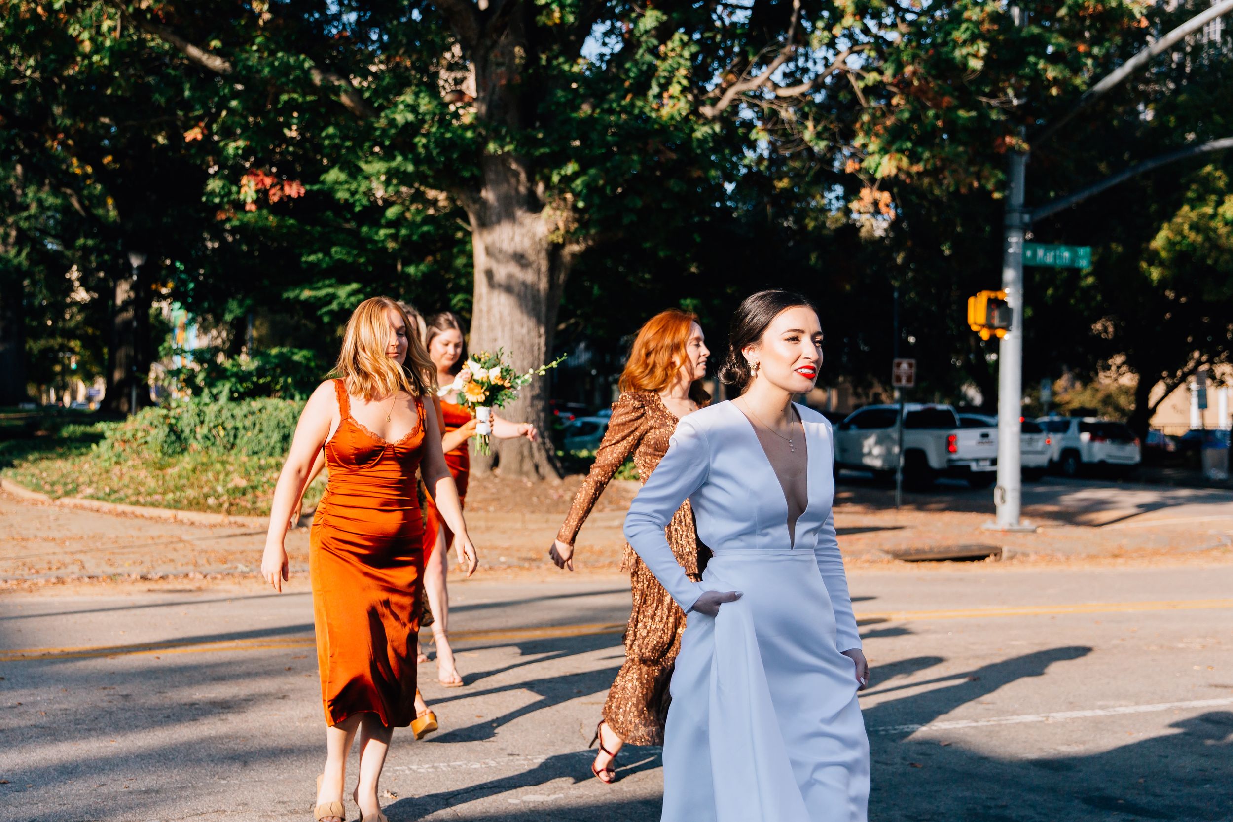 People walking together on a sunny sidewalk path surrounded by lush green trees and foliage.