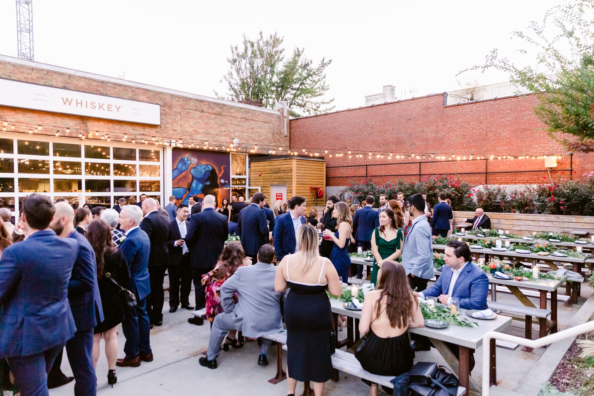 Reception guests mingle in an outdoor brick courtyard with tables and decorations.