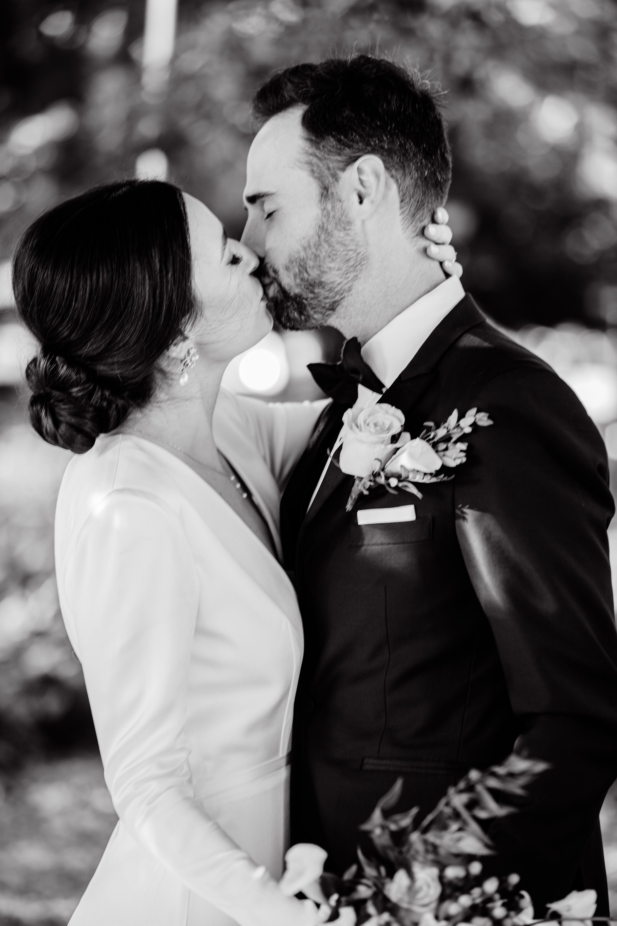 An intimate black and white portrait of newlyweds sharing a romantic kiss outdoors.