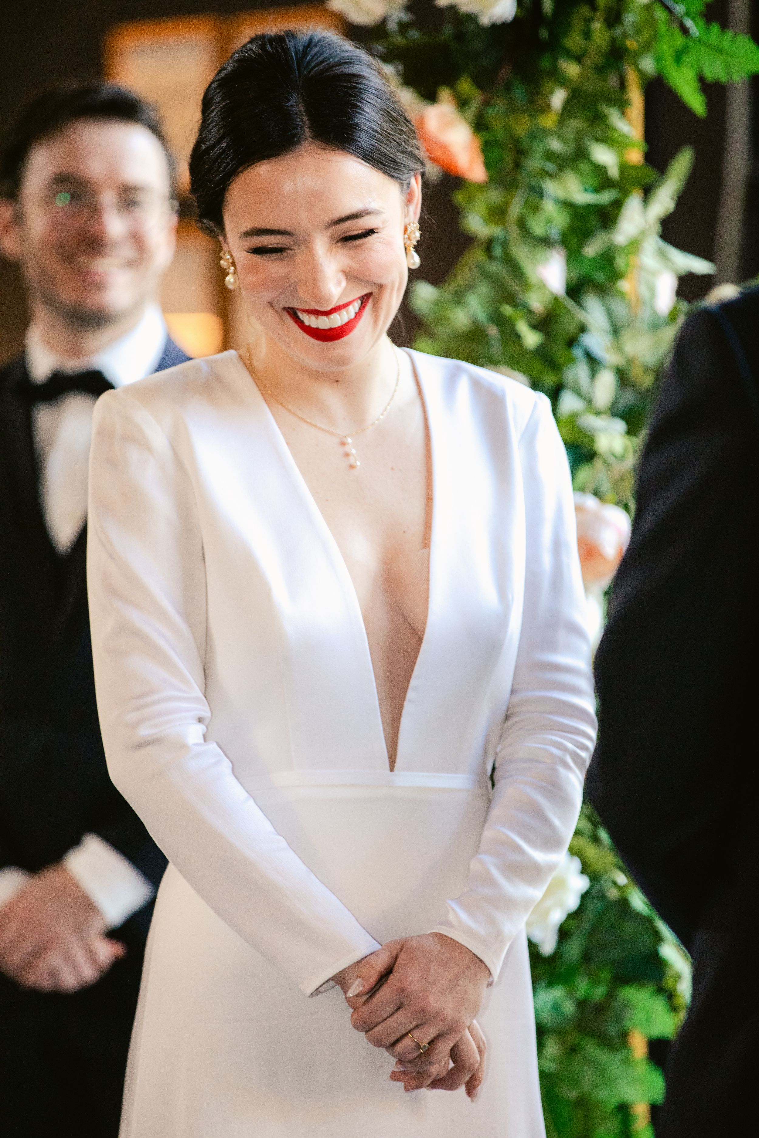 A bride in a modern white long-sleeved gown smiles during her wedding celebration.