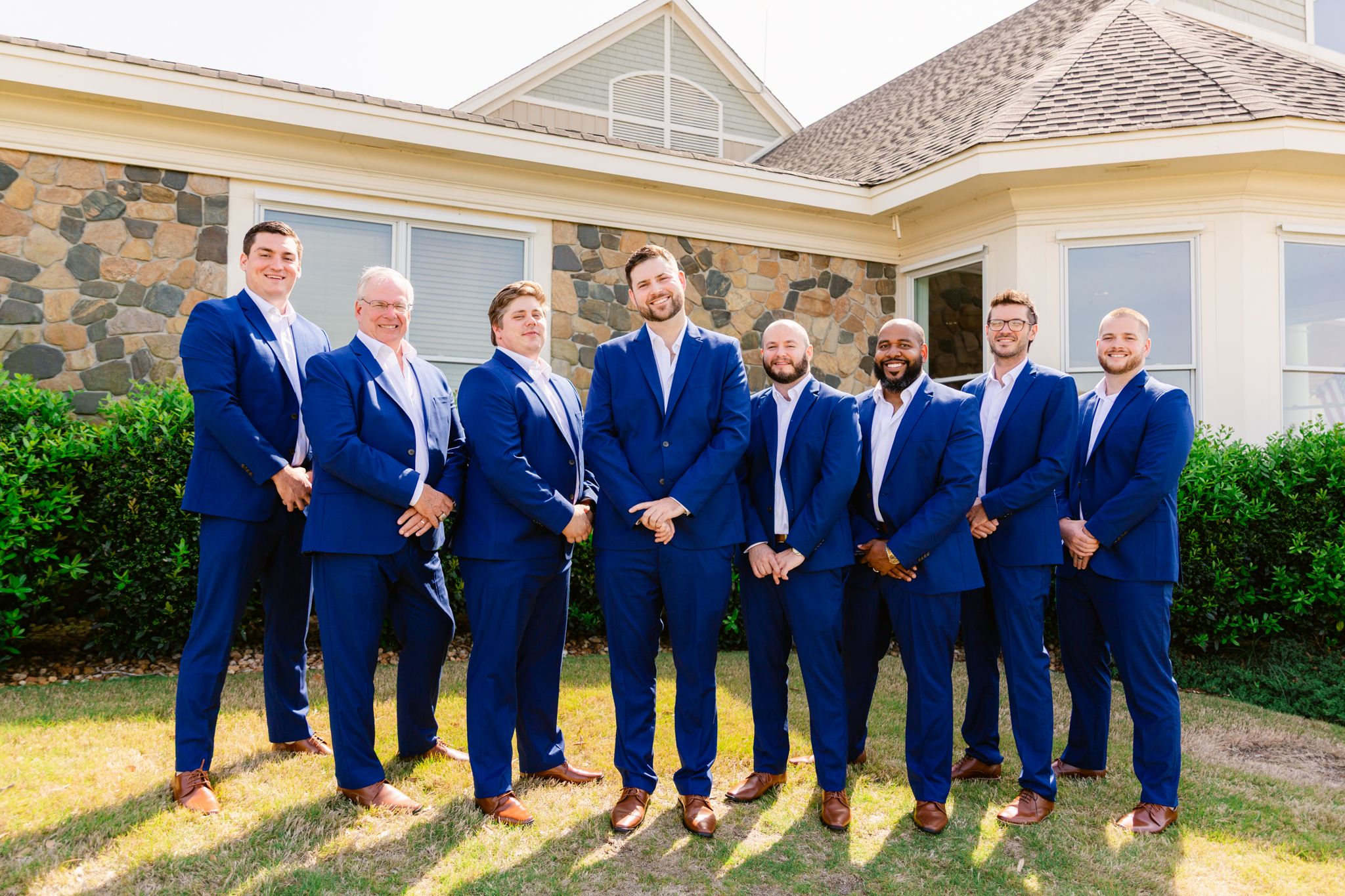 A wedding party in matching navy blue suits poses together in a series of outdoor group photos.