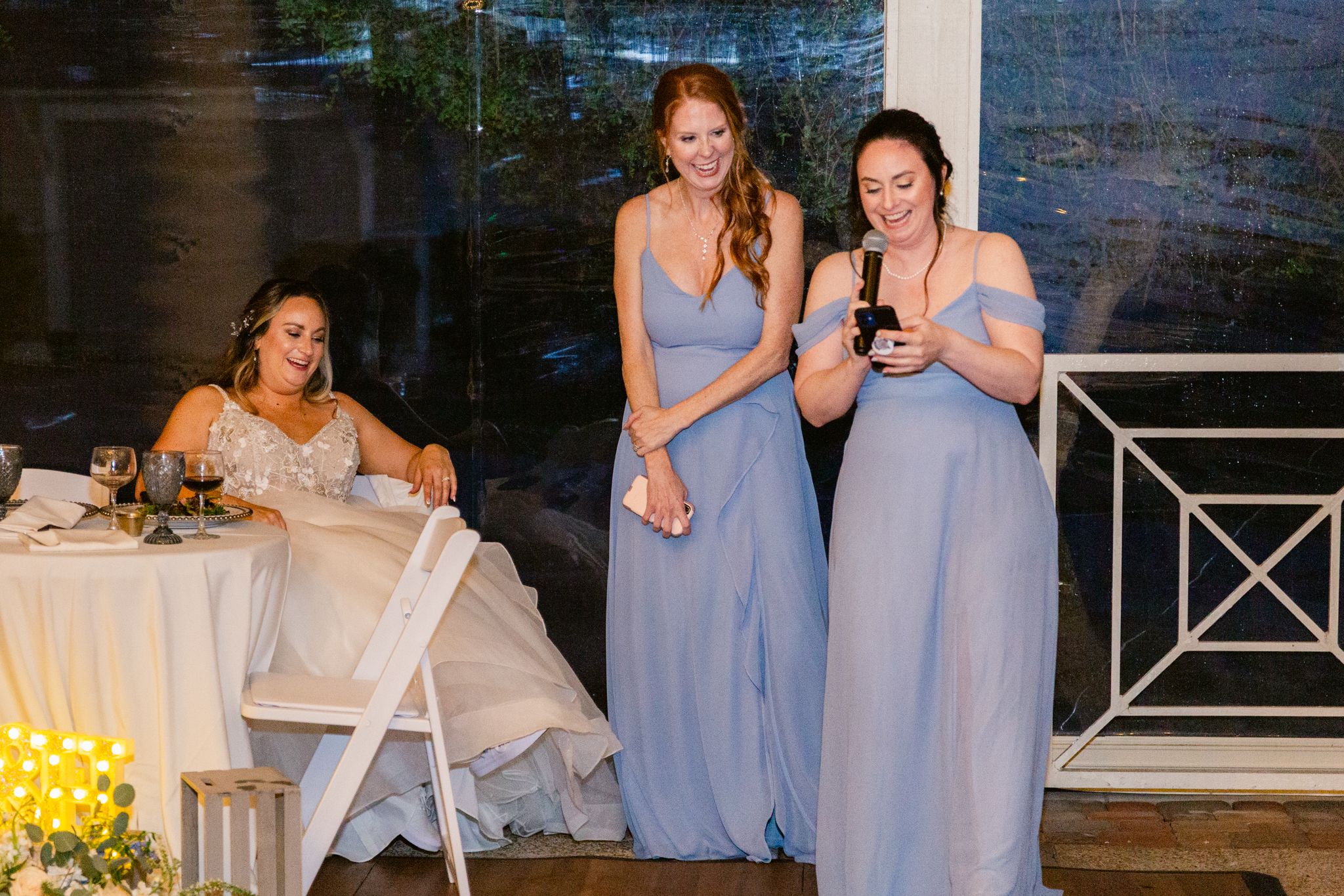 Wedding party in light blue dresses poses together at an outdoor venue with stone walls and floral decor.