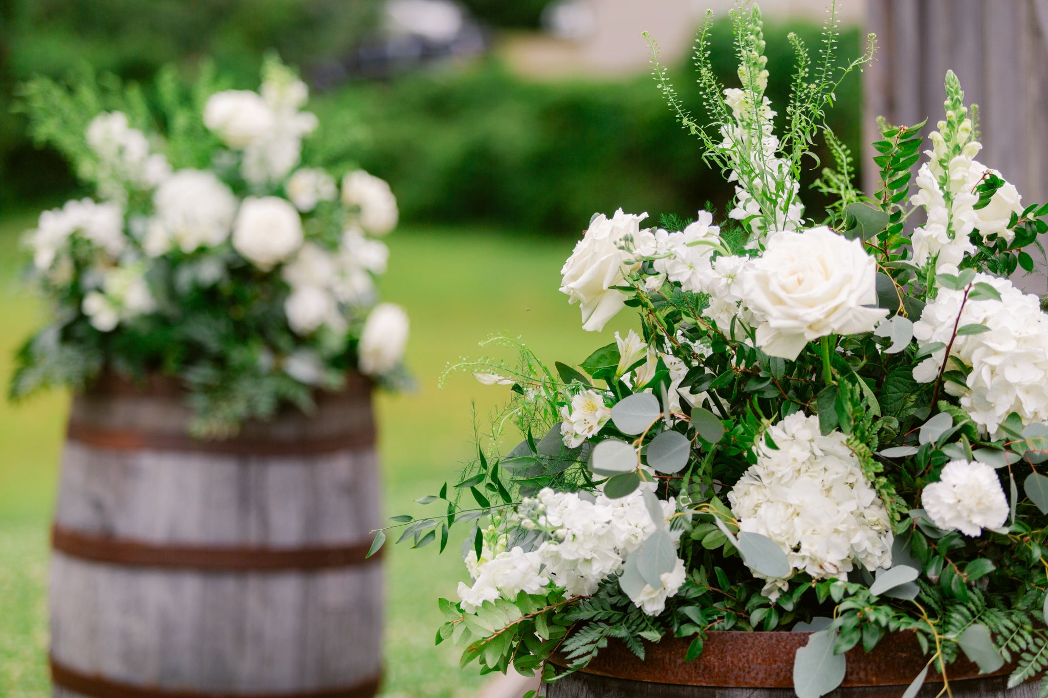 White floral arrangements in rustic wooden barrels create an elegant outdoor garden display.