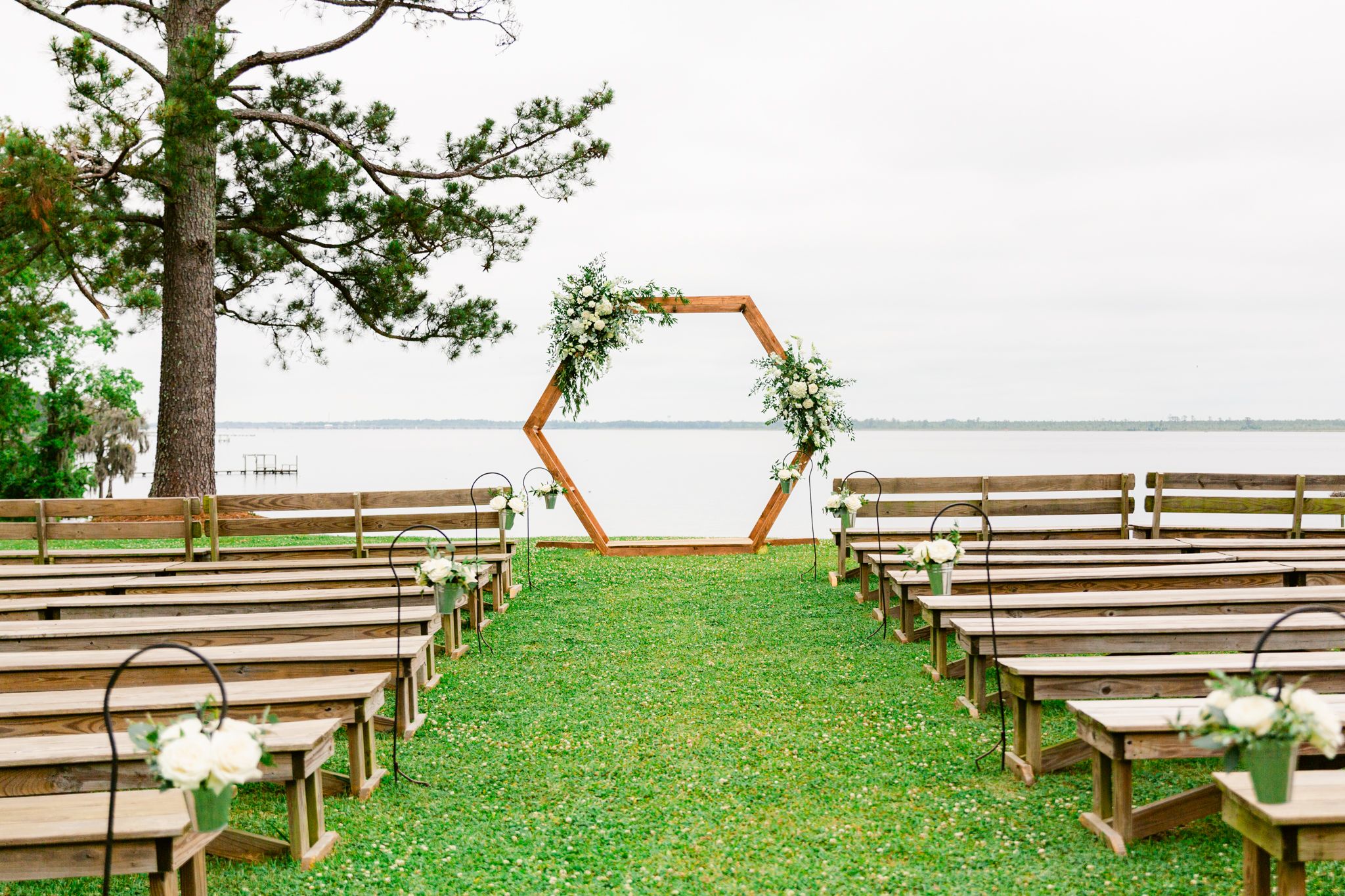 Rustic wooden benches arranged in rows for an outdoor ceremony with a lake view and trees in the background.