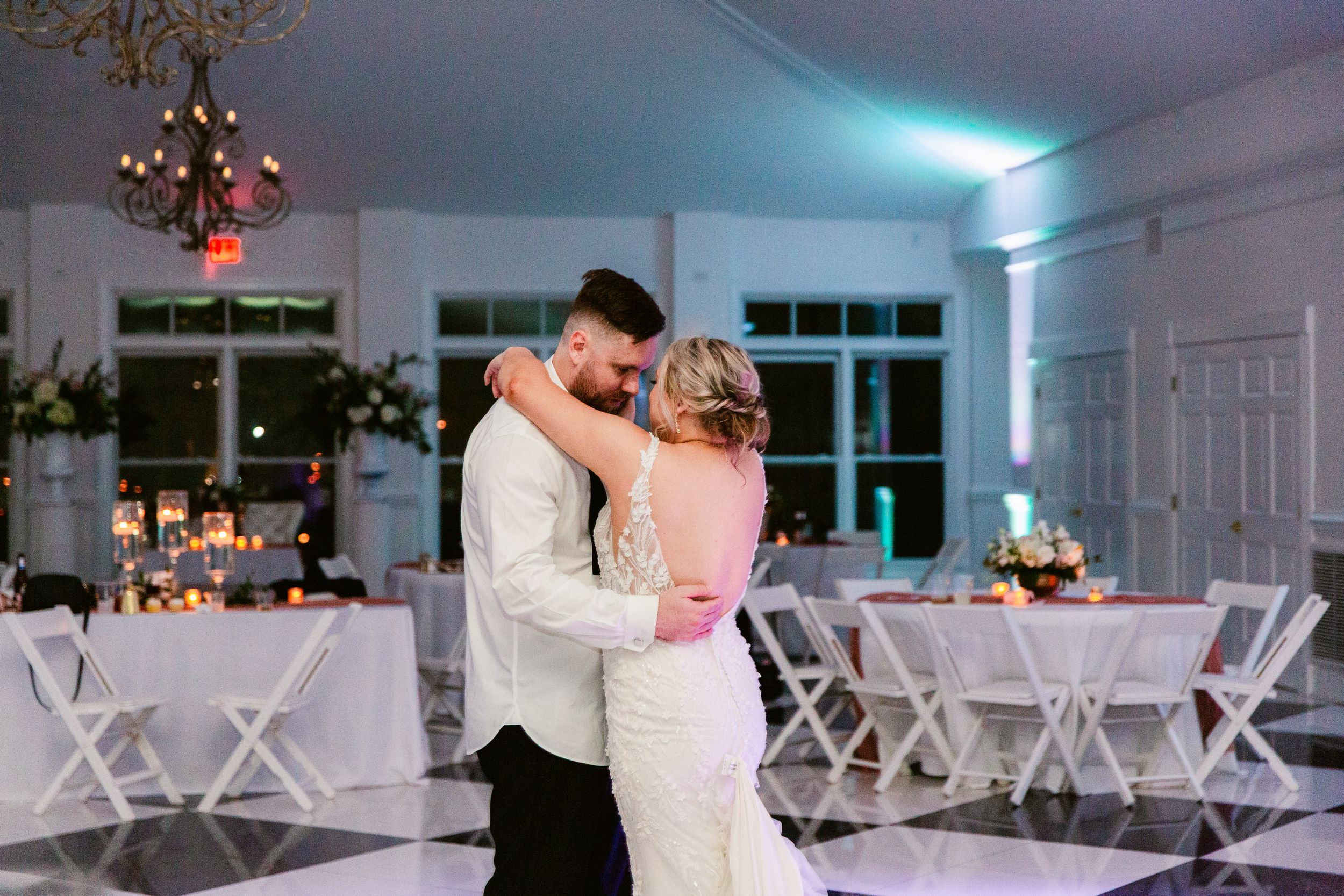 A couple shares their first dance at an elegant wedding reception with white chairs and soft blue lighting.