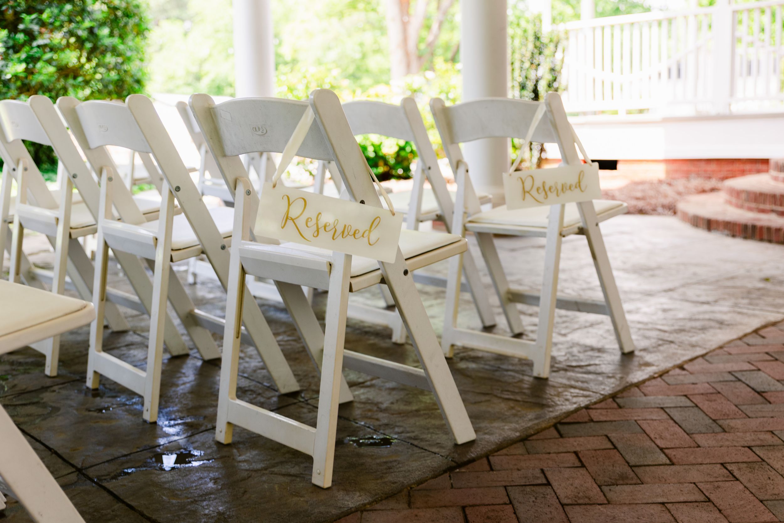 White folding chairs arranged in rows on a brick patio for an outdoor wedding ceremony.