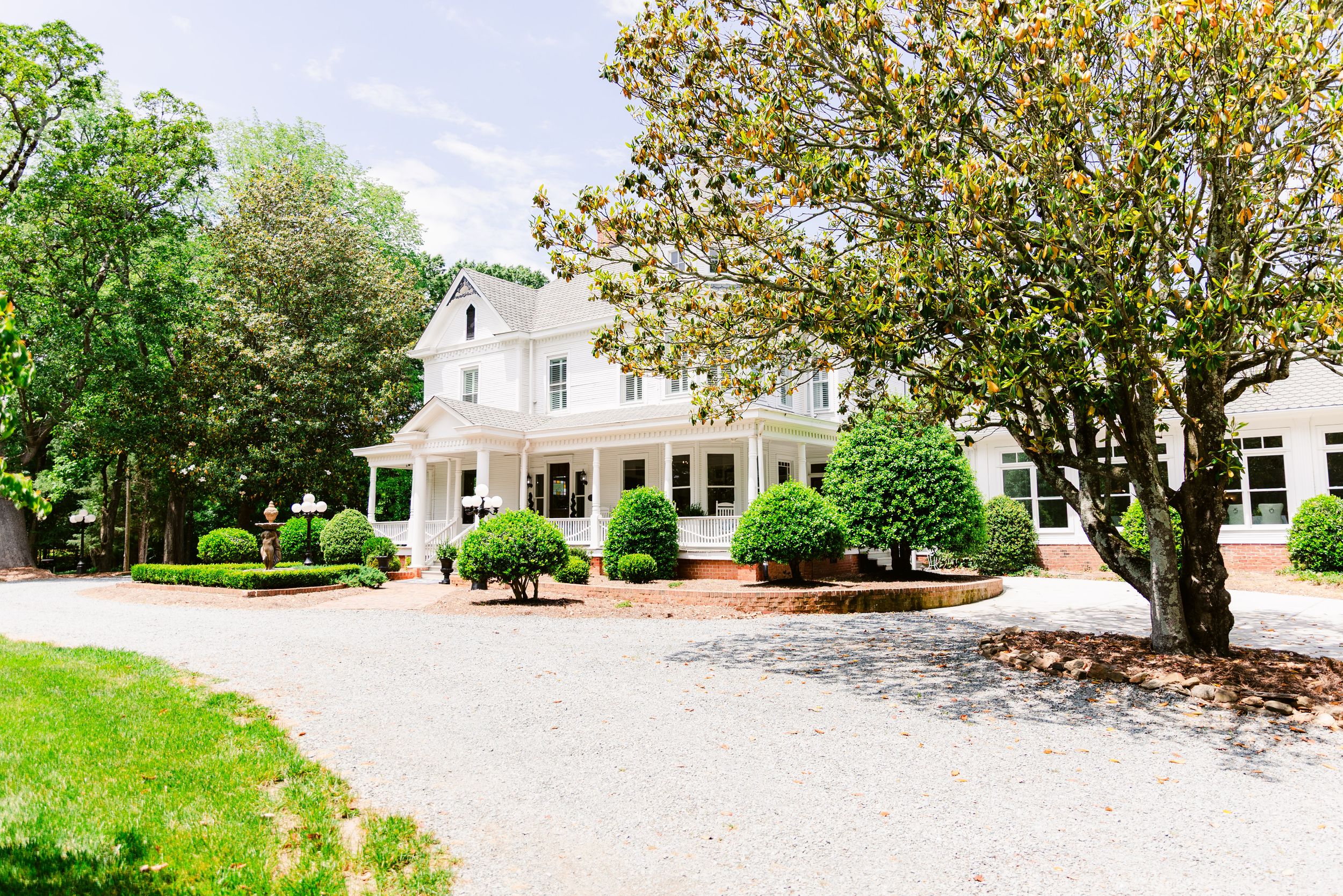 Panoramic view of a white colonial-style house with manicured lawn and landscaping.
