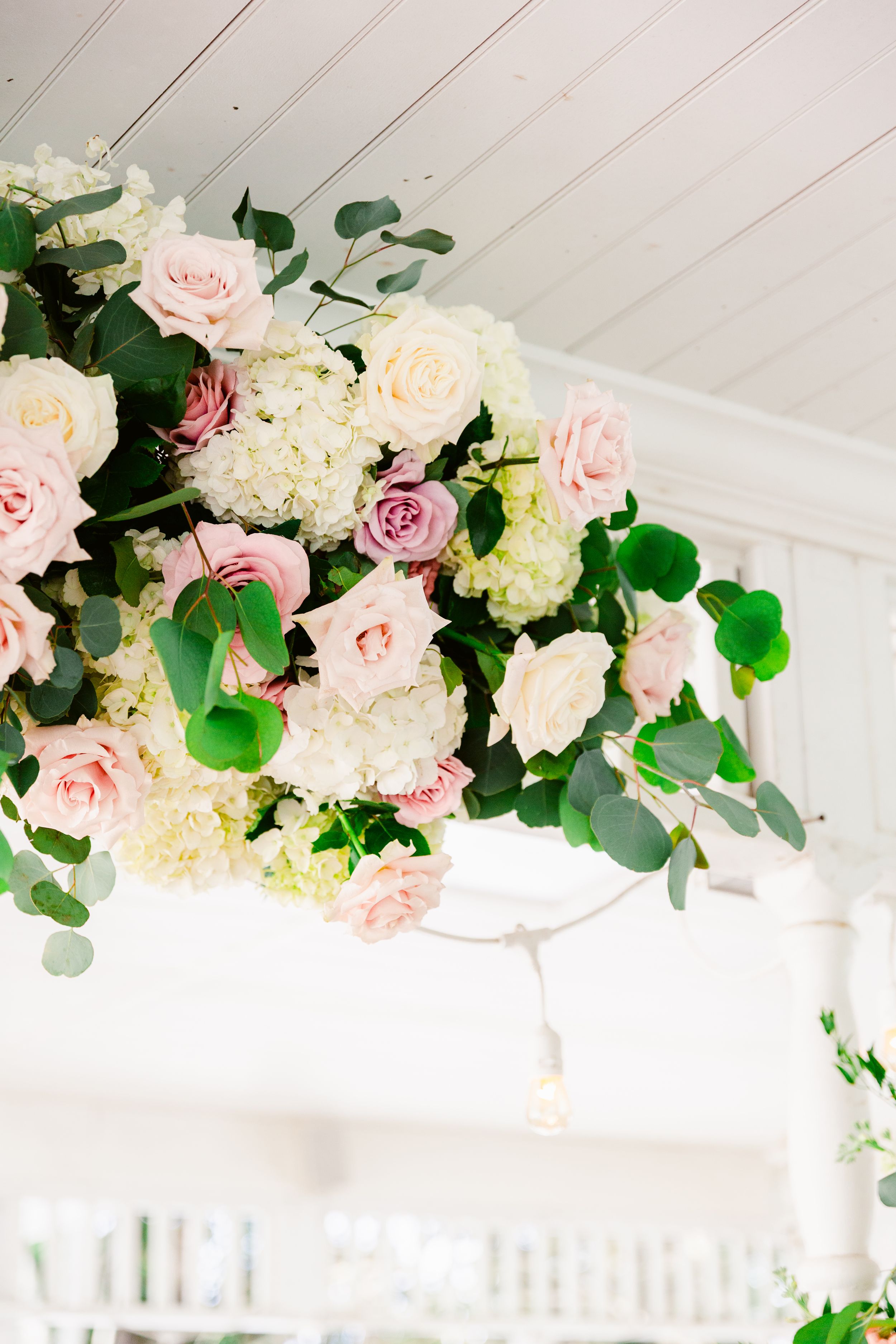 Romantic floral installation with pink roses and eucalyptus adorning a white ceiling beam in an event space.