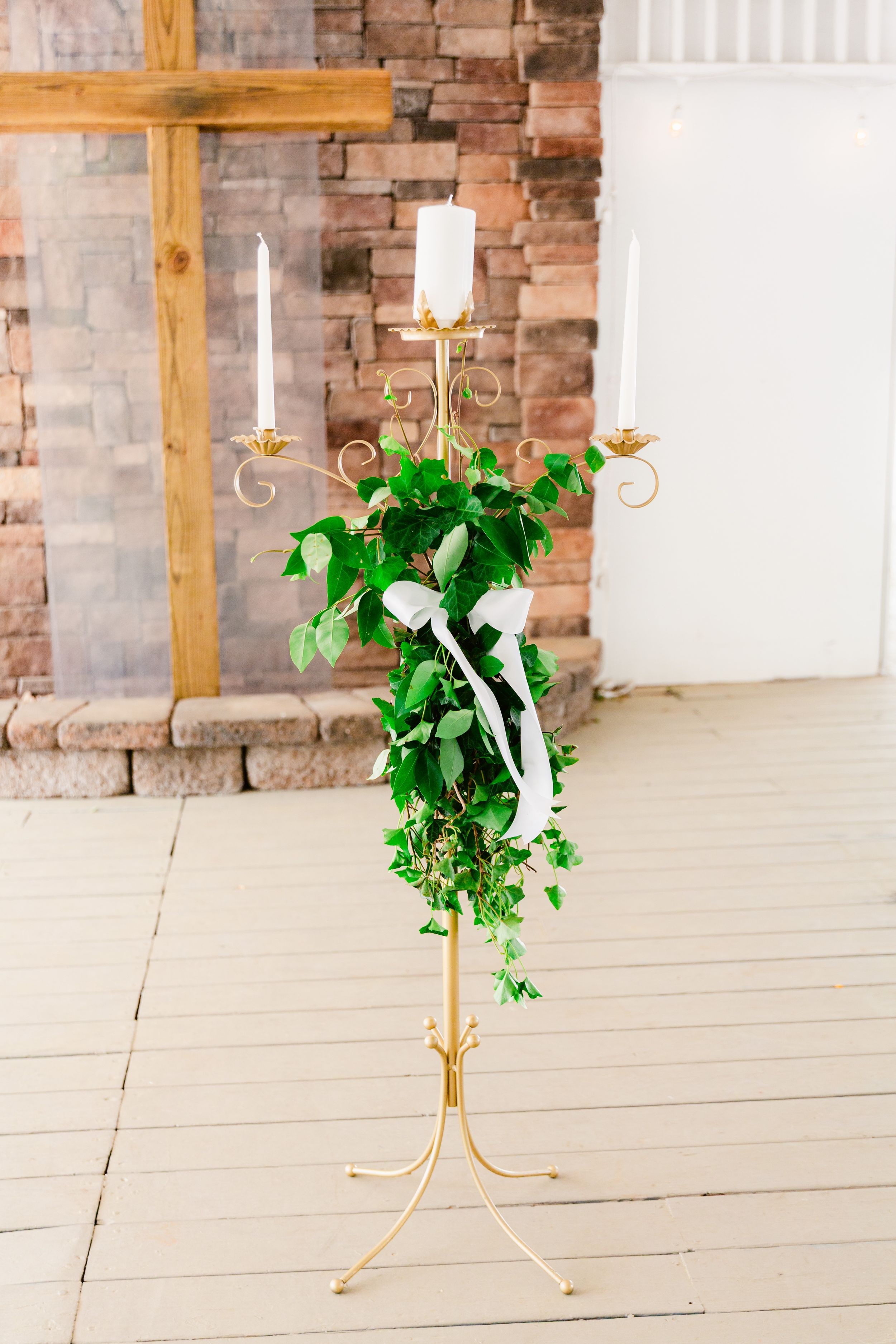 Gold candle holders with greenery arrangements against exposed brick walls in an event space.