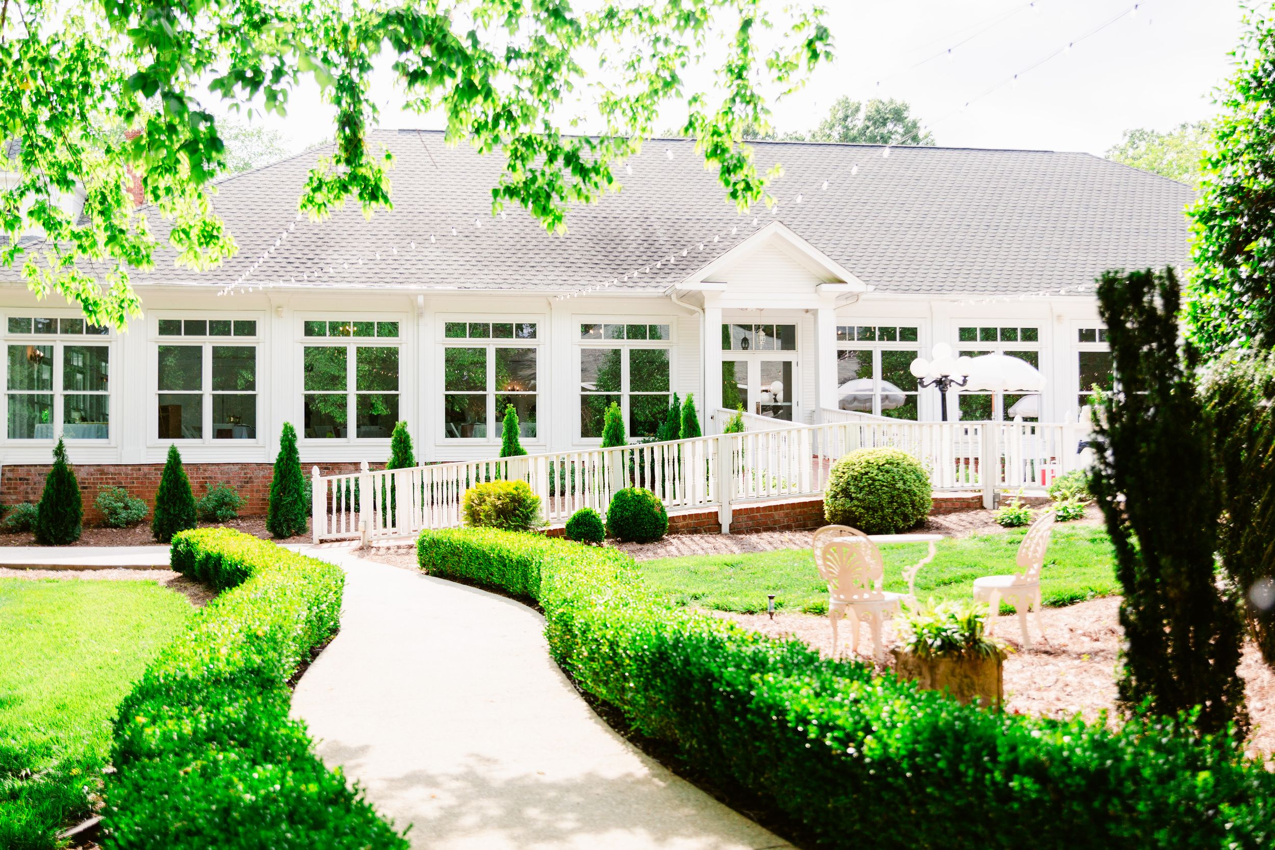 White event venue building with large windows and landscaped gardens in a lush green setting.