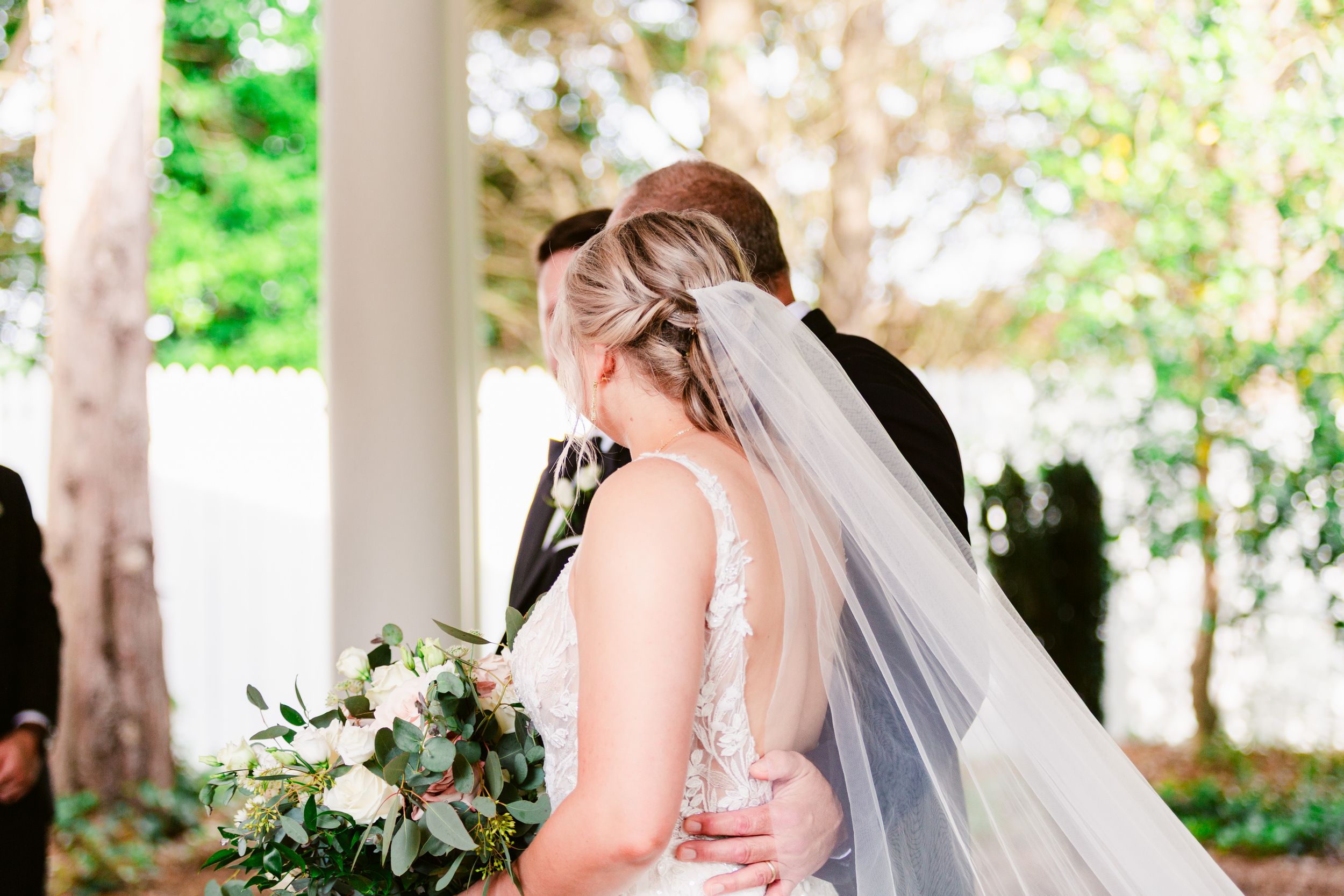 A bride and groom share an intimate moment under a white gazebo surrounded by lush greenery.