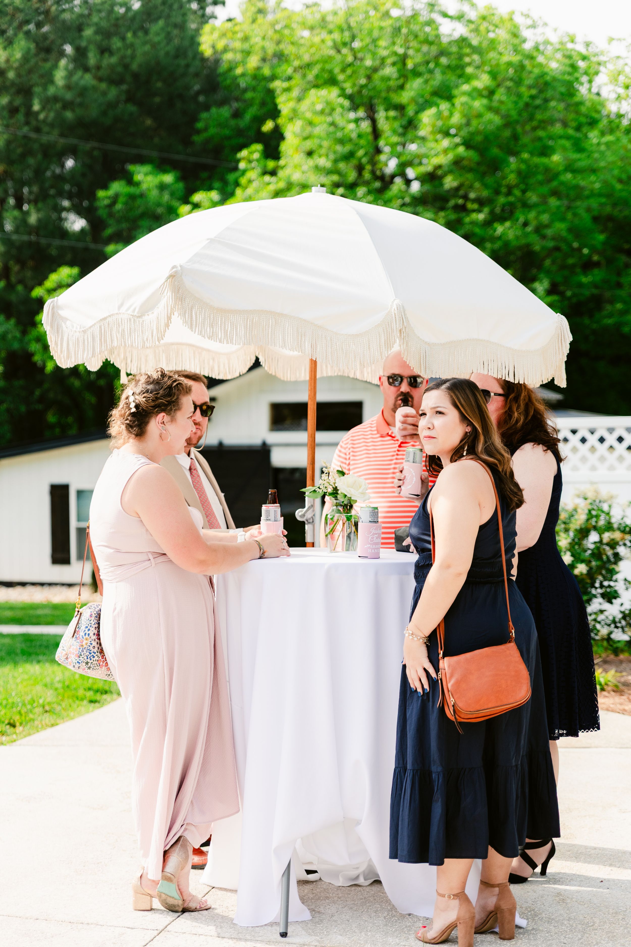 Party guests gather under white parasols at outdoor cocktail tables during a summer event.
