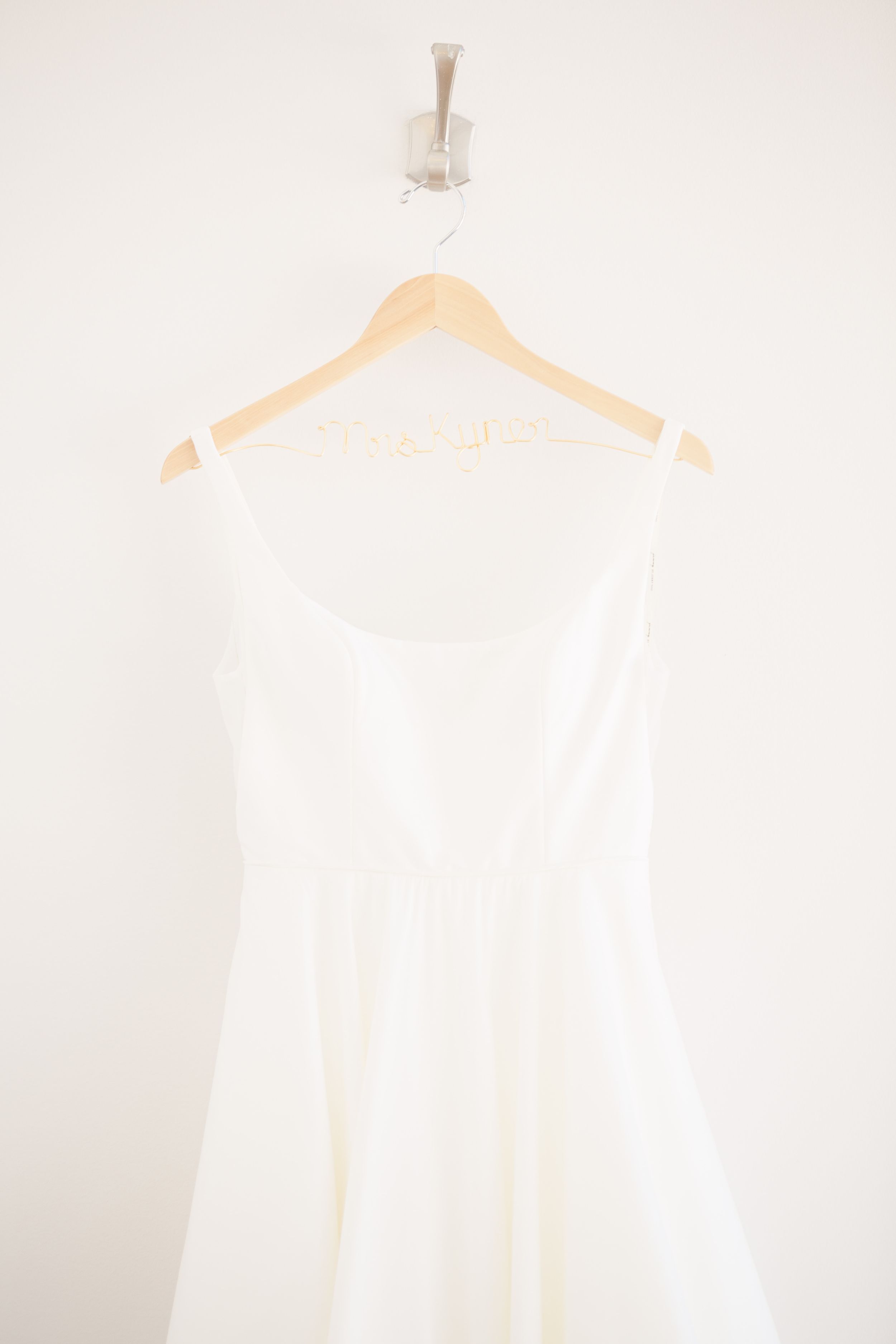 White wedding dress hanging on wooden hanger against light background.