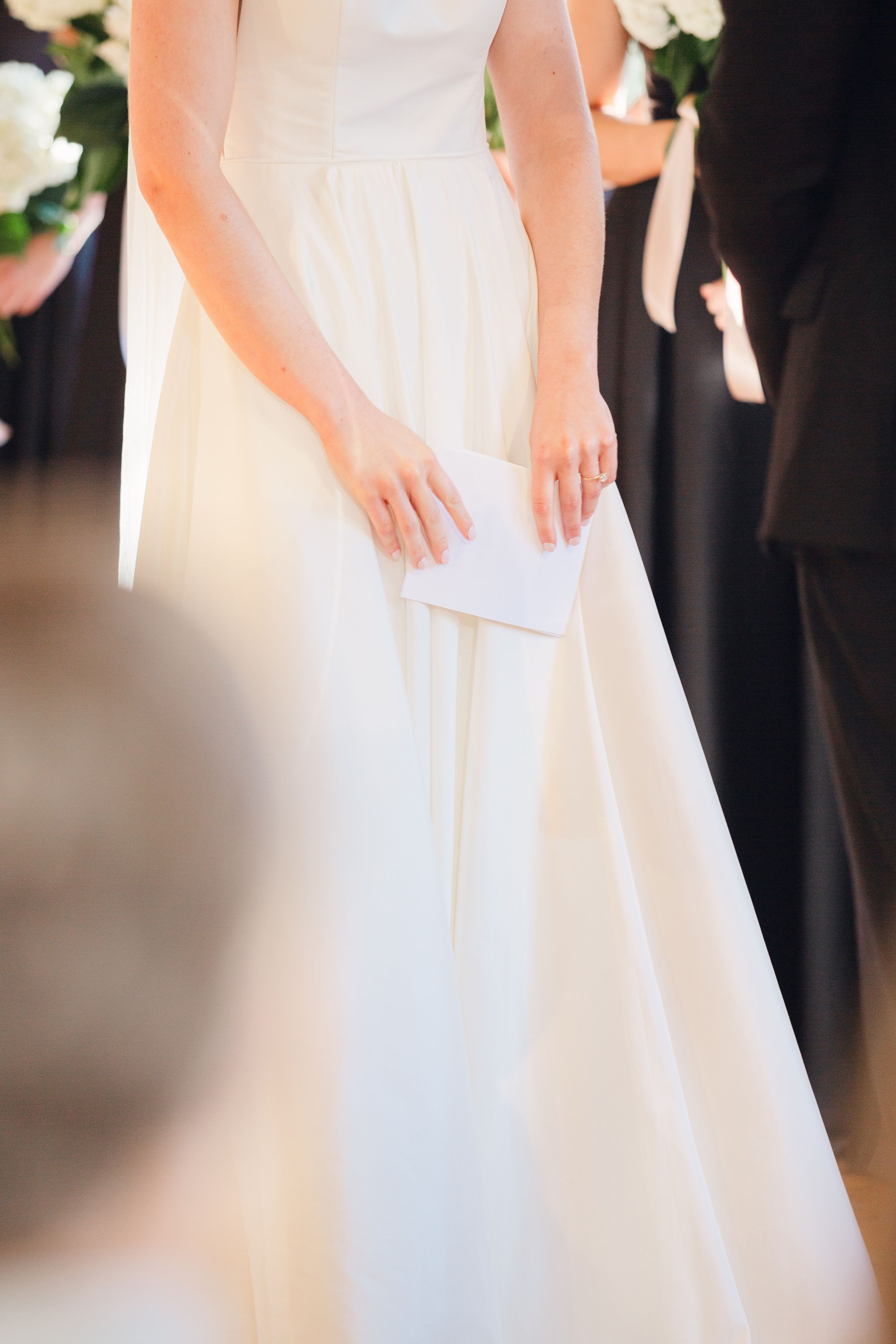 A close-up view of a white wedding dress and hands holding a paper during a ceremony.