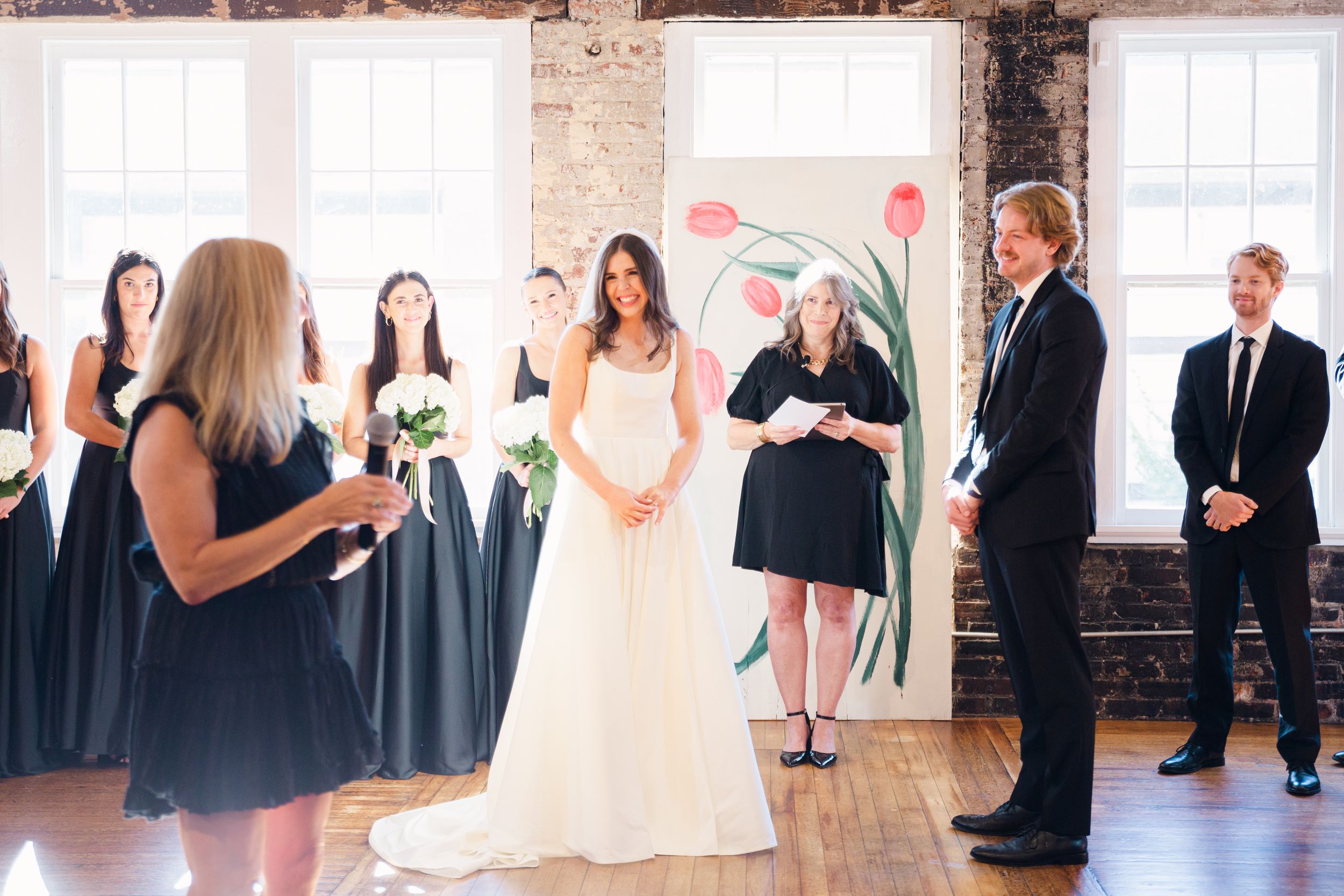 A wedding ceremony in progress with attendants in navy dresses and decorative floral artwork.