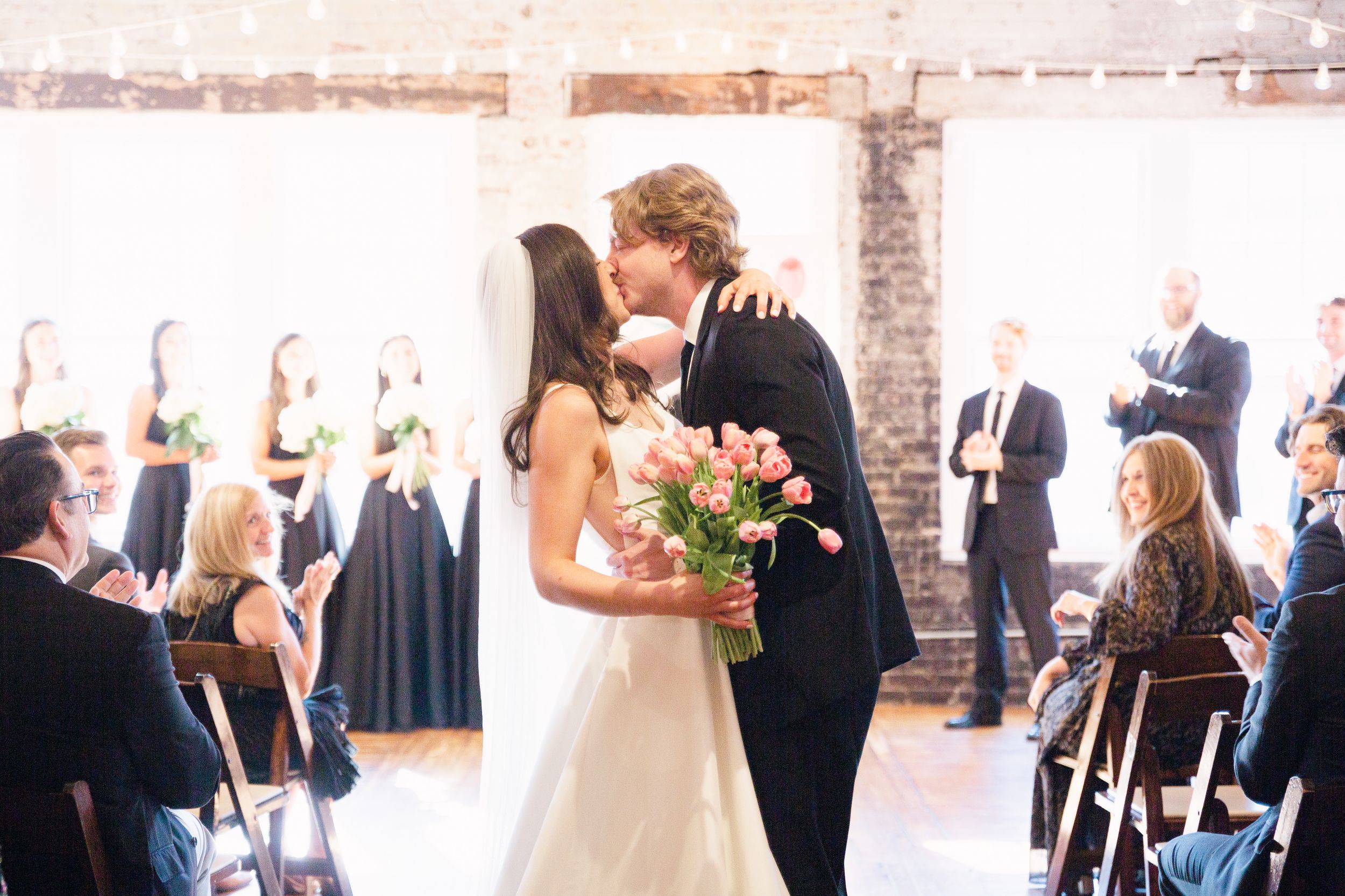 A wedding ceremony in a rustic brick-walled venue with guests seated in rows.