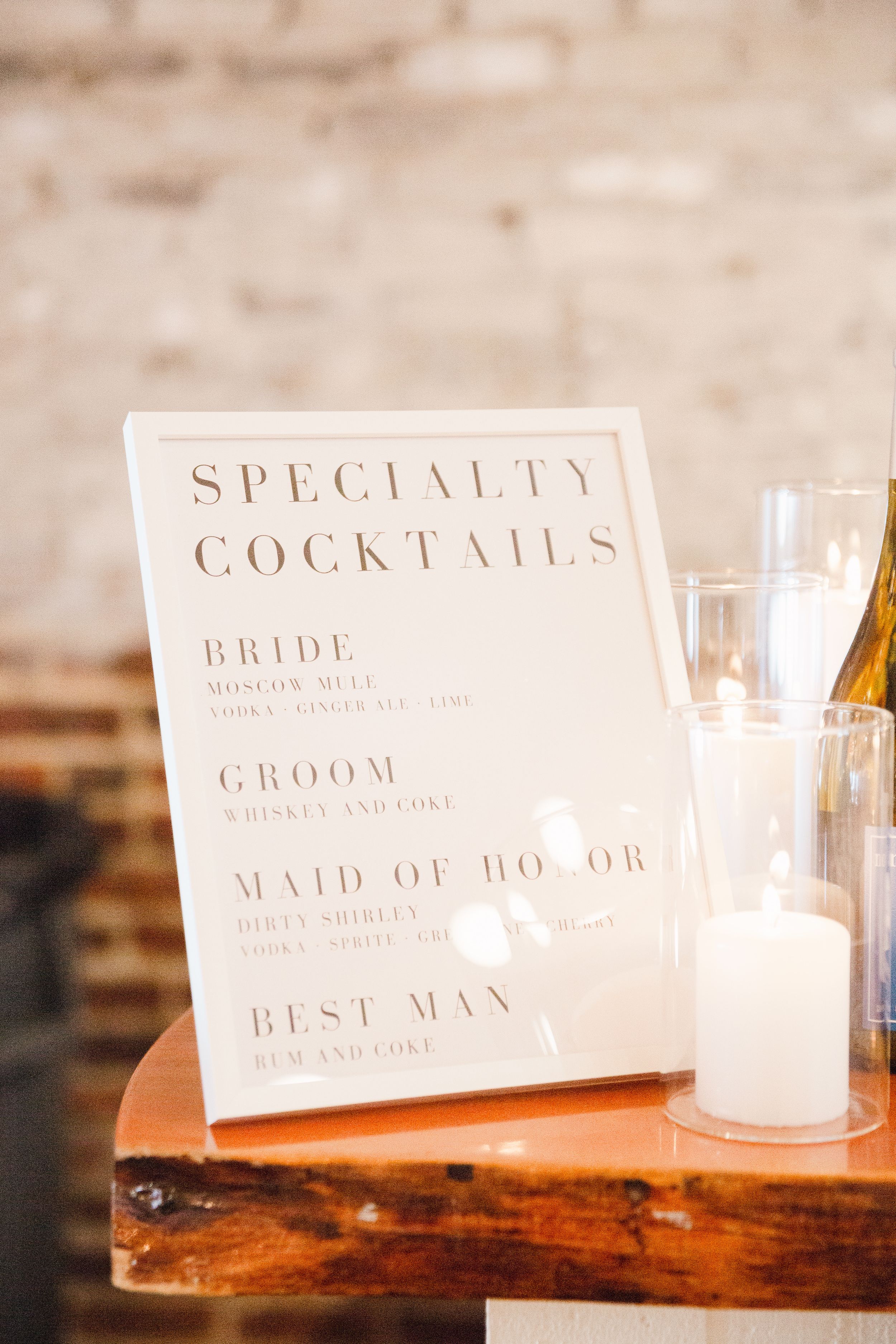 Specialty cocktails menu sign for wedding party displayed on wooden surface.