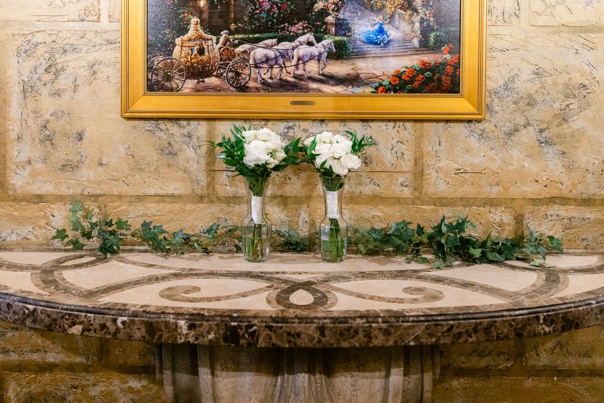 Rustic stone wall with decorative framed artwork and greenery creating an elegant outdoor gallery setting.