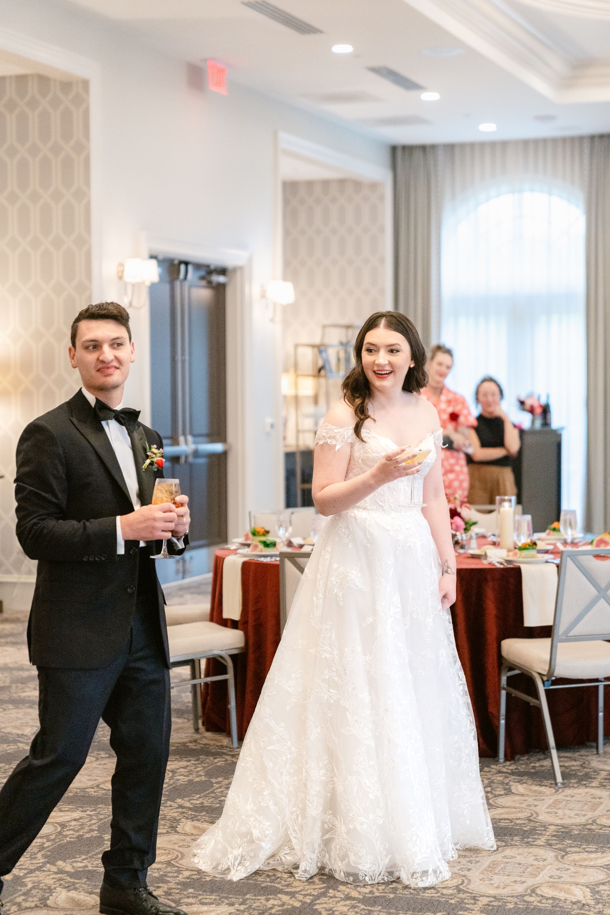 Elegant wedding reception in a bright ballroom with white decor and floral arrangements.