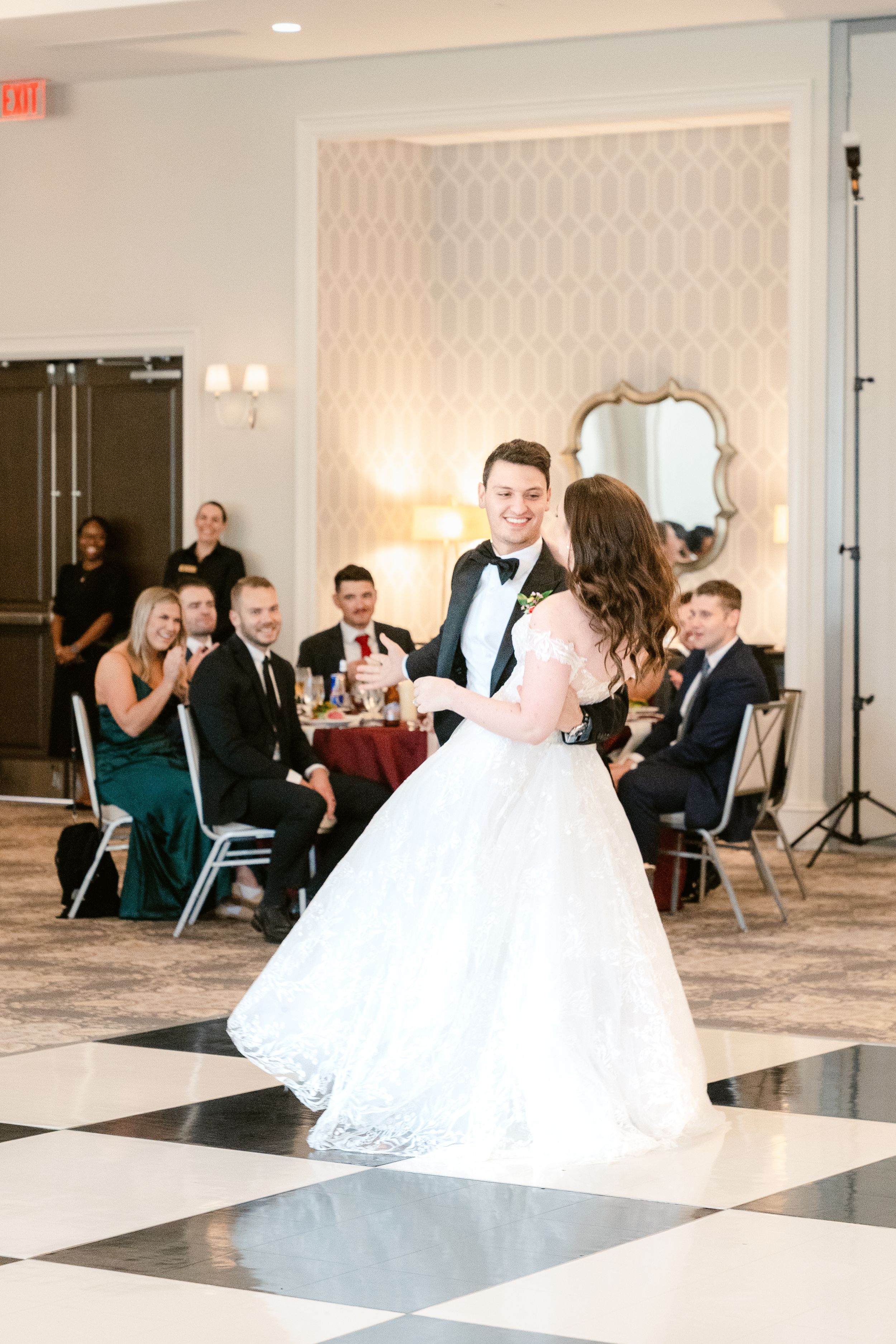Wedding party dances and celebrates in an elegant ballroom with black and white checkered floor.