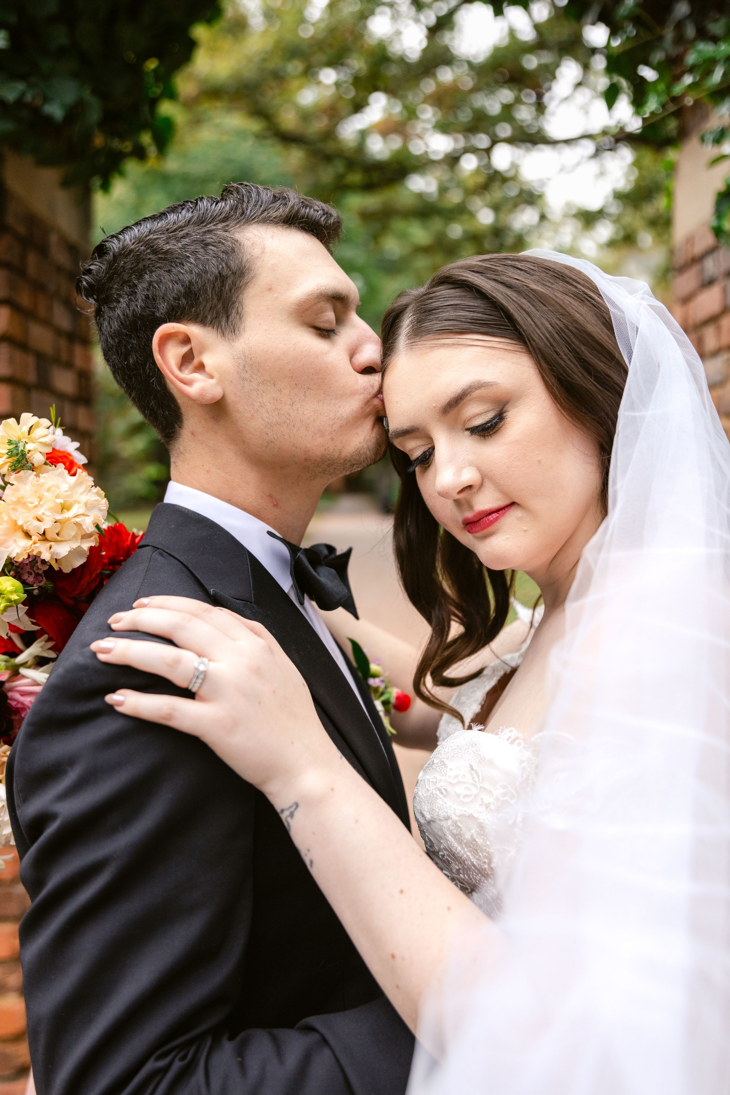 A romantic wedding couple embracing in an outdoor garden setting with lush greenery in the background.