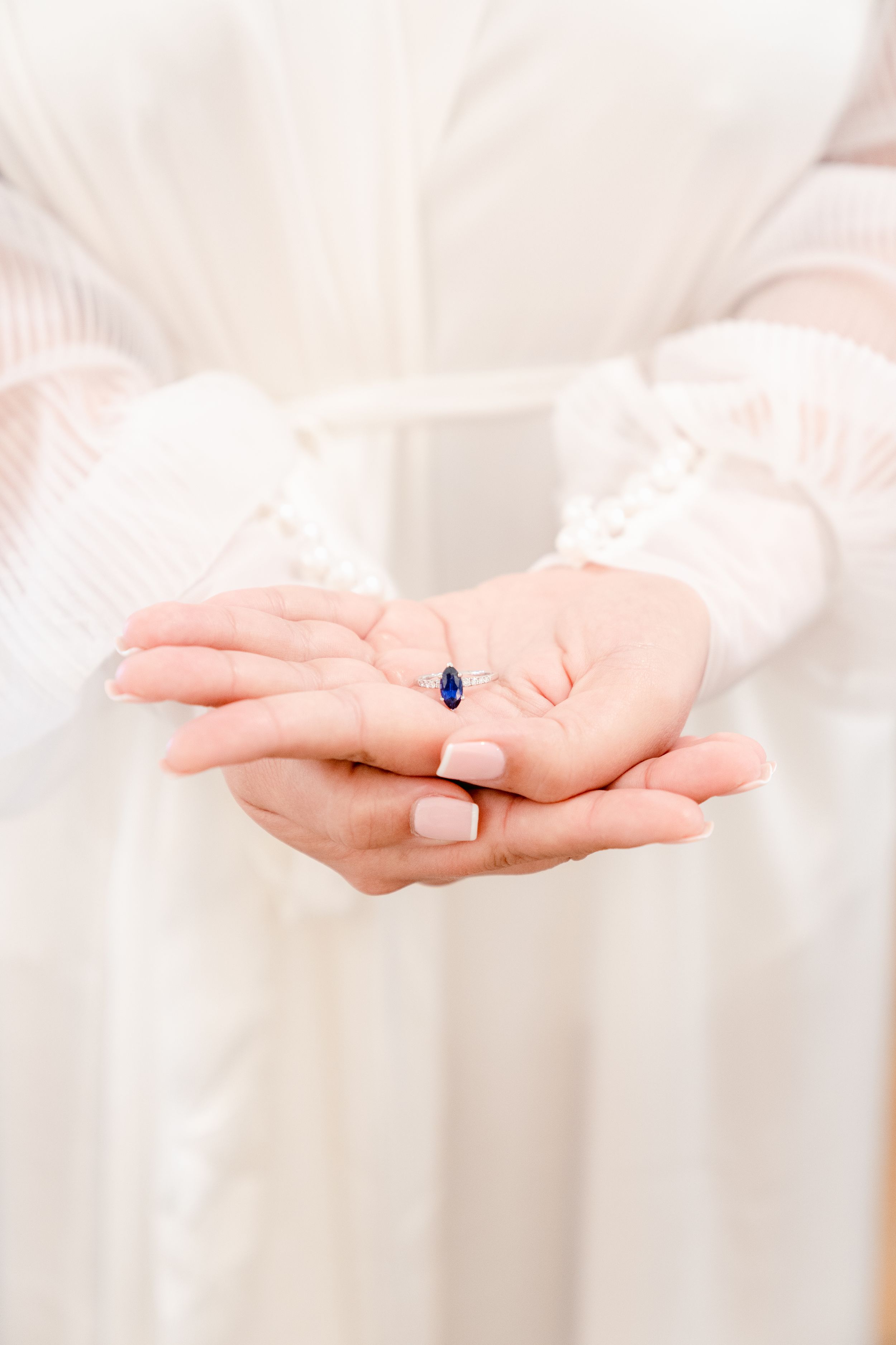 Elegant blue gemstone ring presented in open palms against white fabric background.