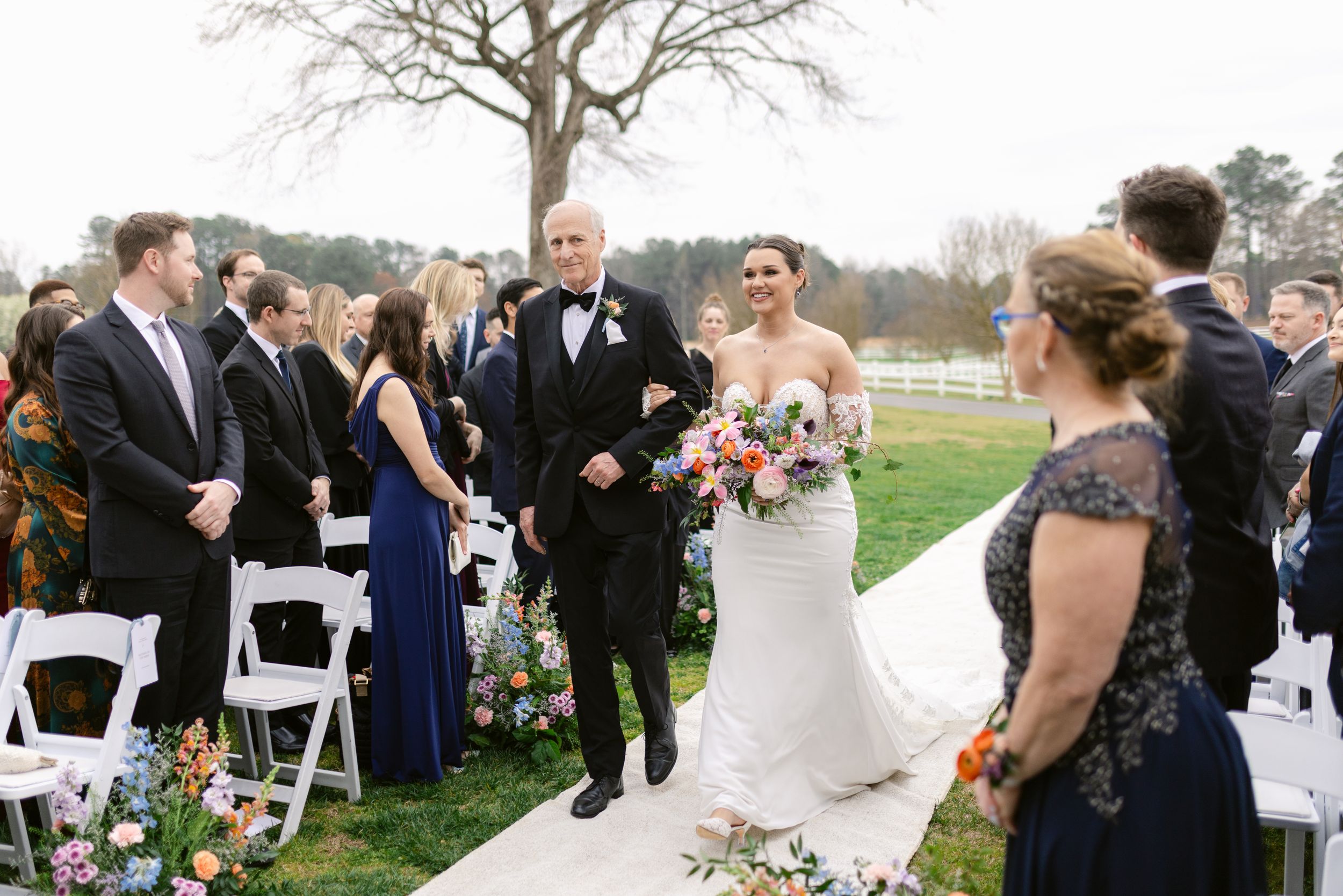 Wedding ceremony celebration outdoors with decorated aisle and white chairs on a grassy lawn.