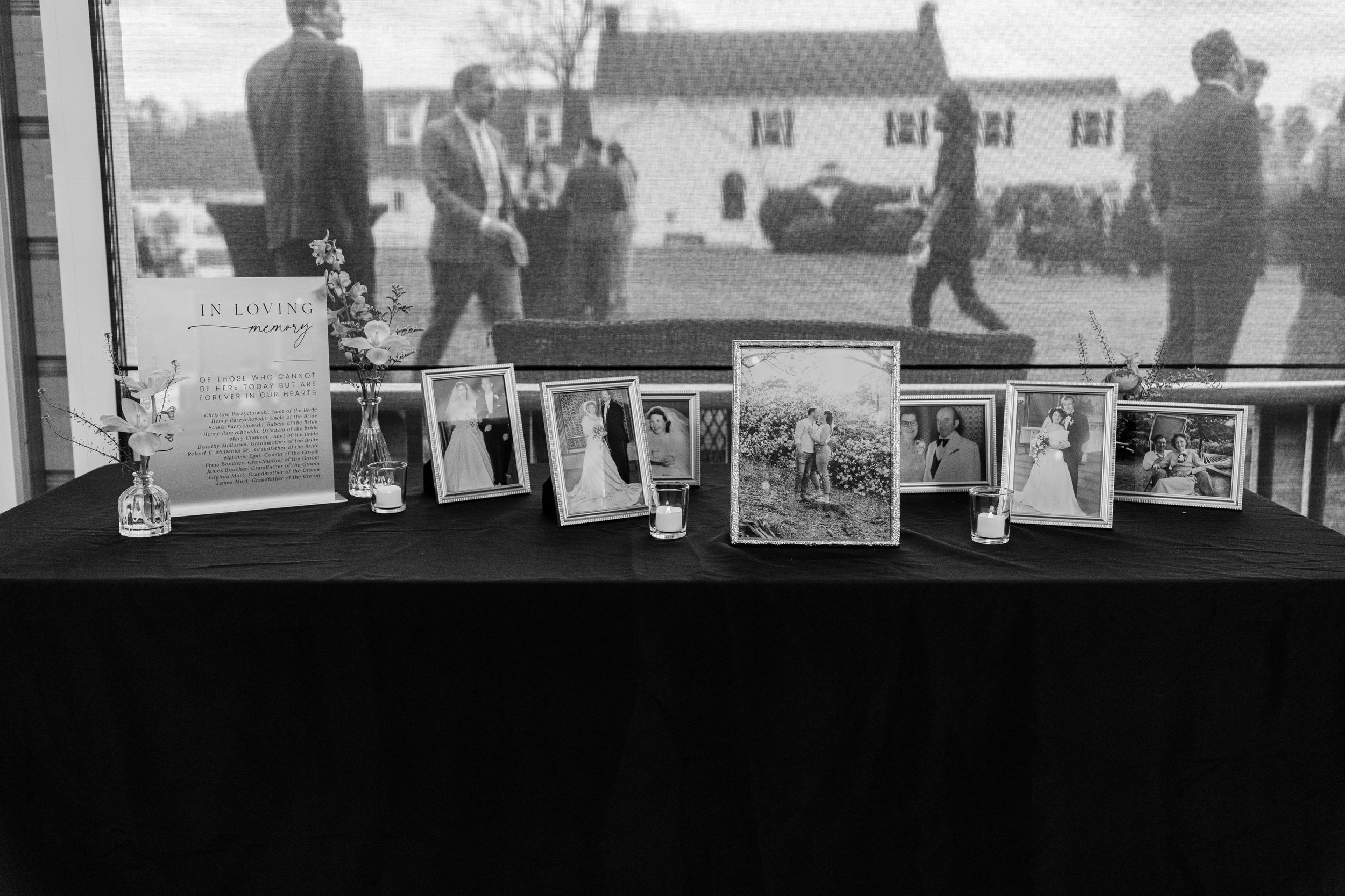 Black and white photograph showing vintage family photos displayed in frames on a dark table surface.