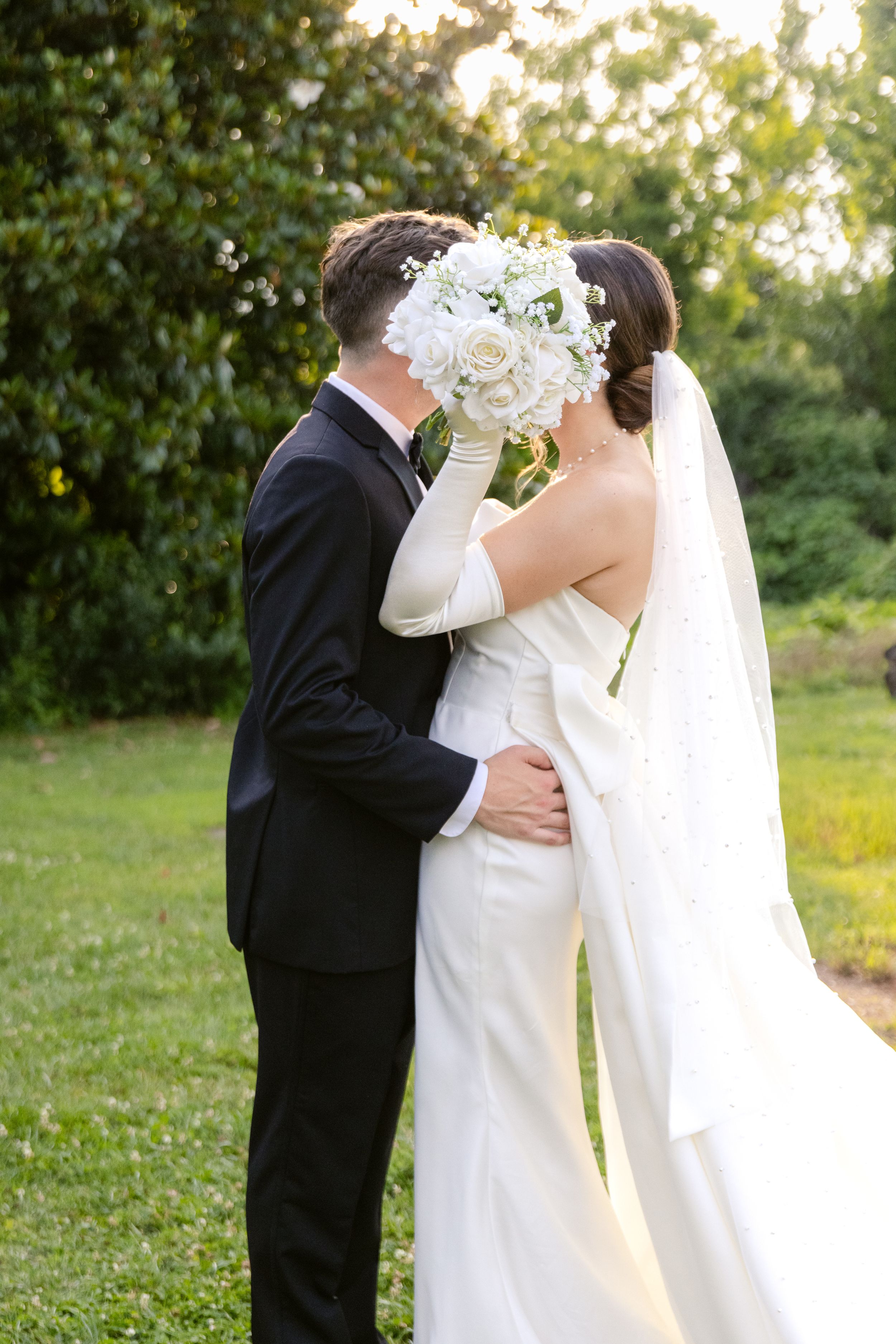 A romantic wedding moment captured at sunset with a white bridal bouquet held between the couple.